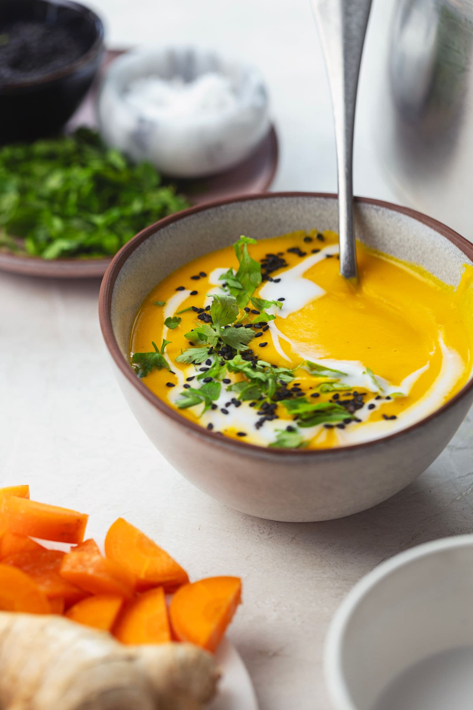 Close-up of silky carrot soup topped with coconut milk, fresh herbs, and toasted seeds.