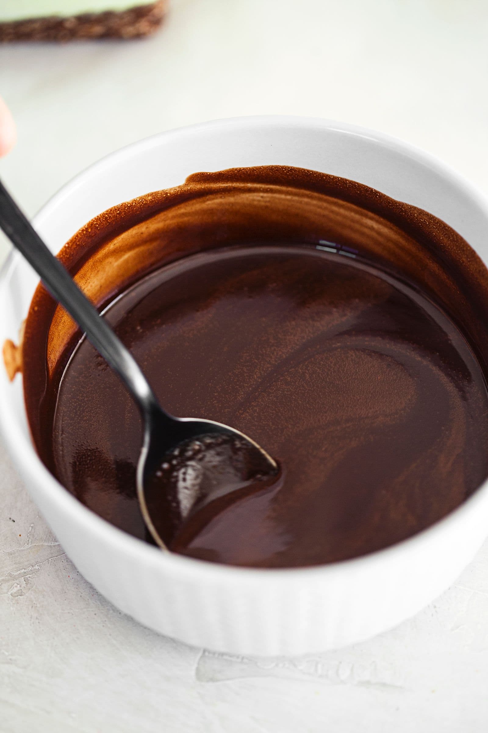 Close-up of glossy, melted chocolate mixture in a white bowl.