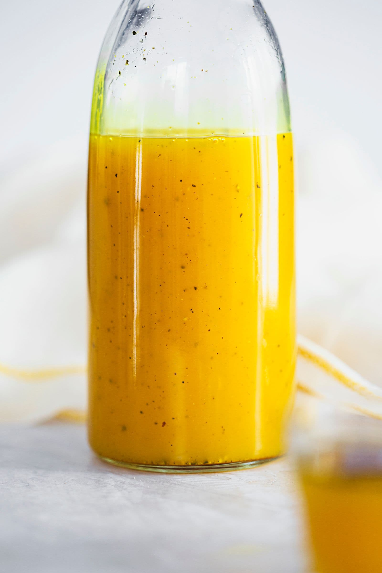 Homemade ginger and turmeric syrup in a tall glass bottle with dark specks of pepper.