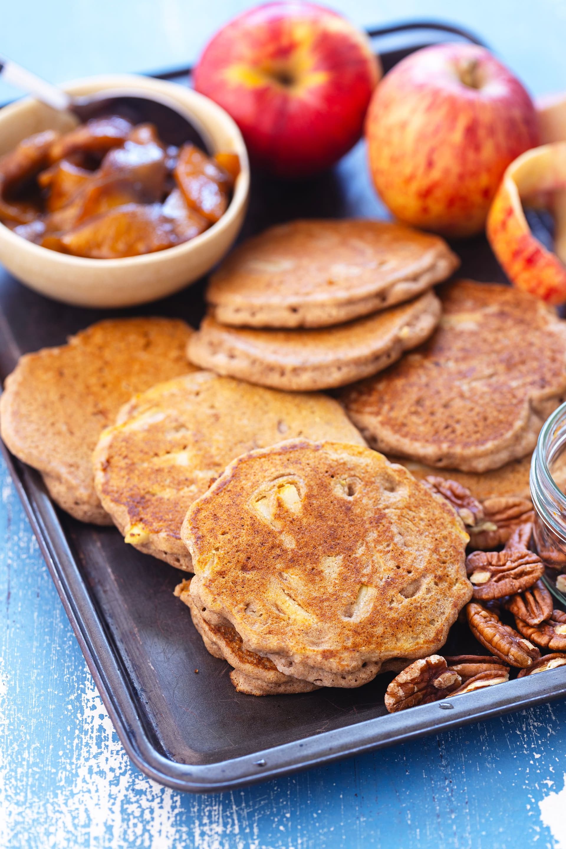 Golden buckwheat pancakes on tray with pecans and whole apples around.