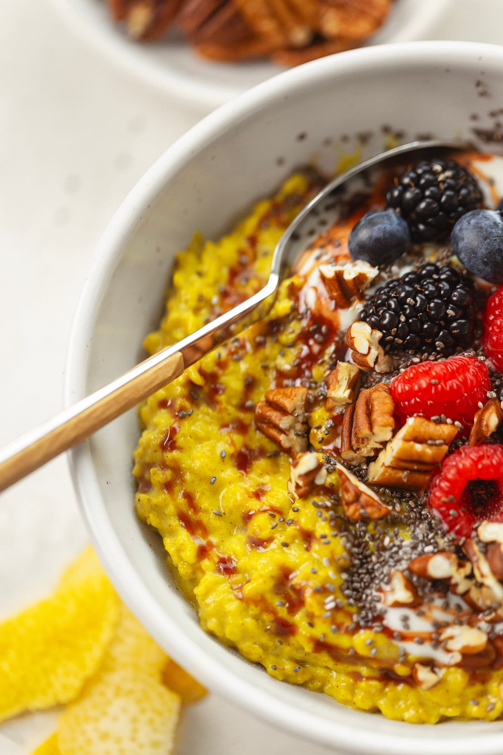 Creamy turmeric oatmeal topped with raspberries, blackberries, blueberries, date syrup, chia seeds and pecans, close-up in a ceramic bowl