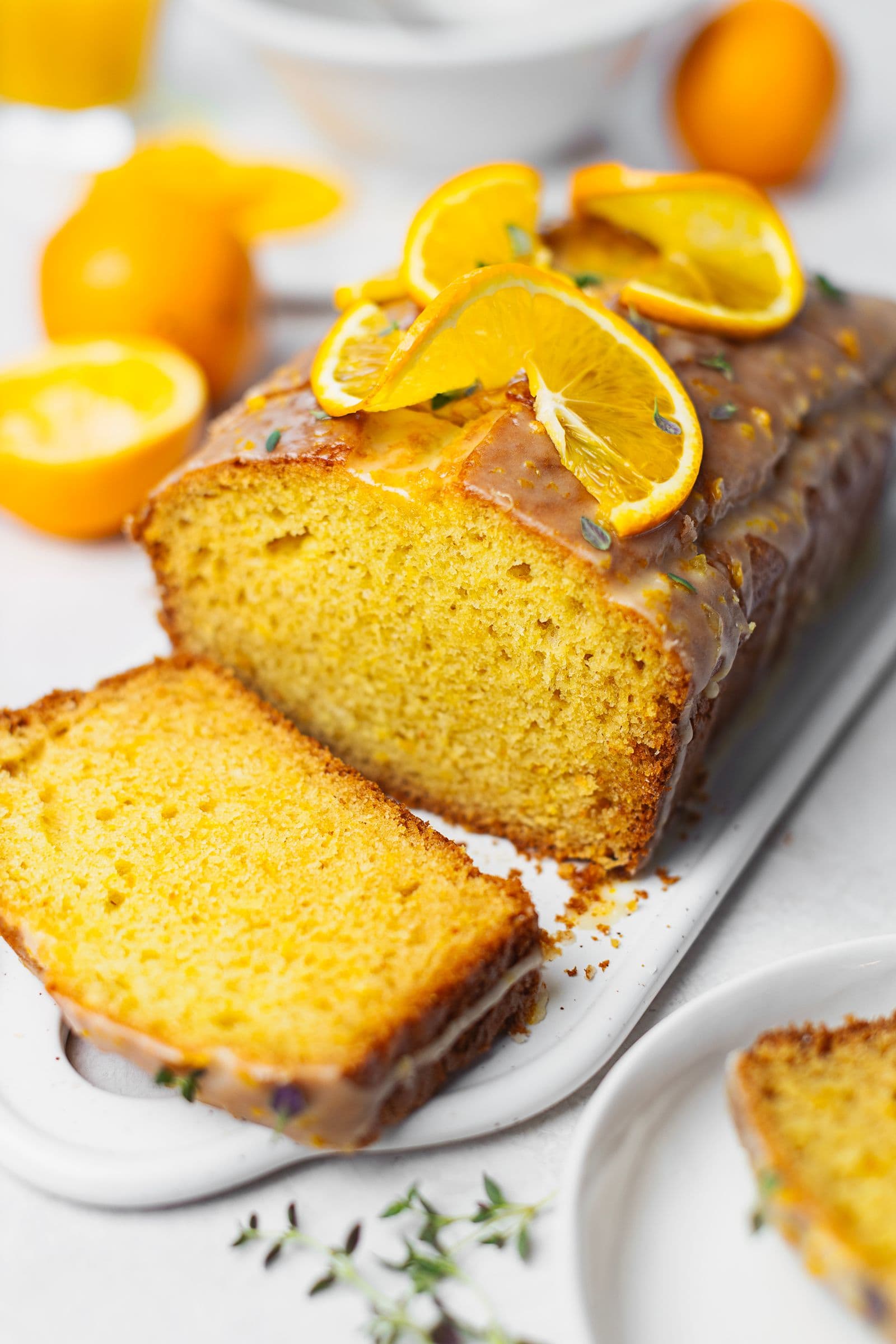 Sliced orange loaf cake with glaze, topped with orange and thyme, showing its golden fluffy texture.