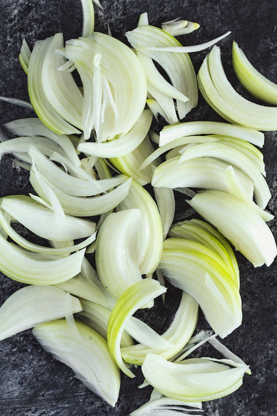 Fresh onions sliced thinly on a dark background, ready for cooking.