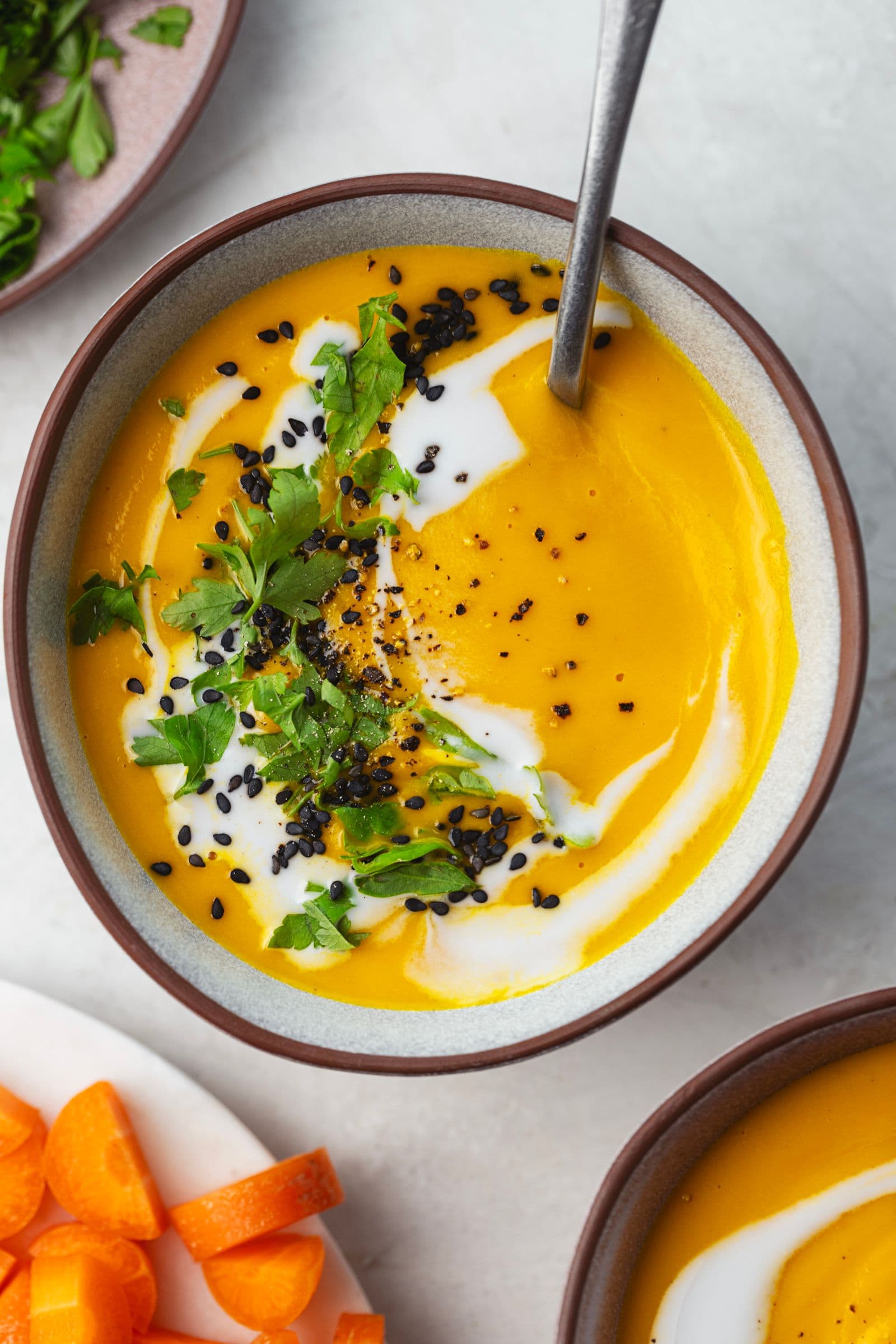 Bowl of carrot soup finished with coconut milk, fresh parsley, black seeds, and freshly ground pepper.