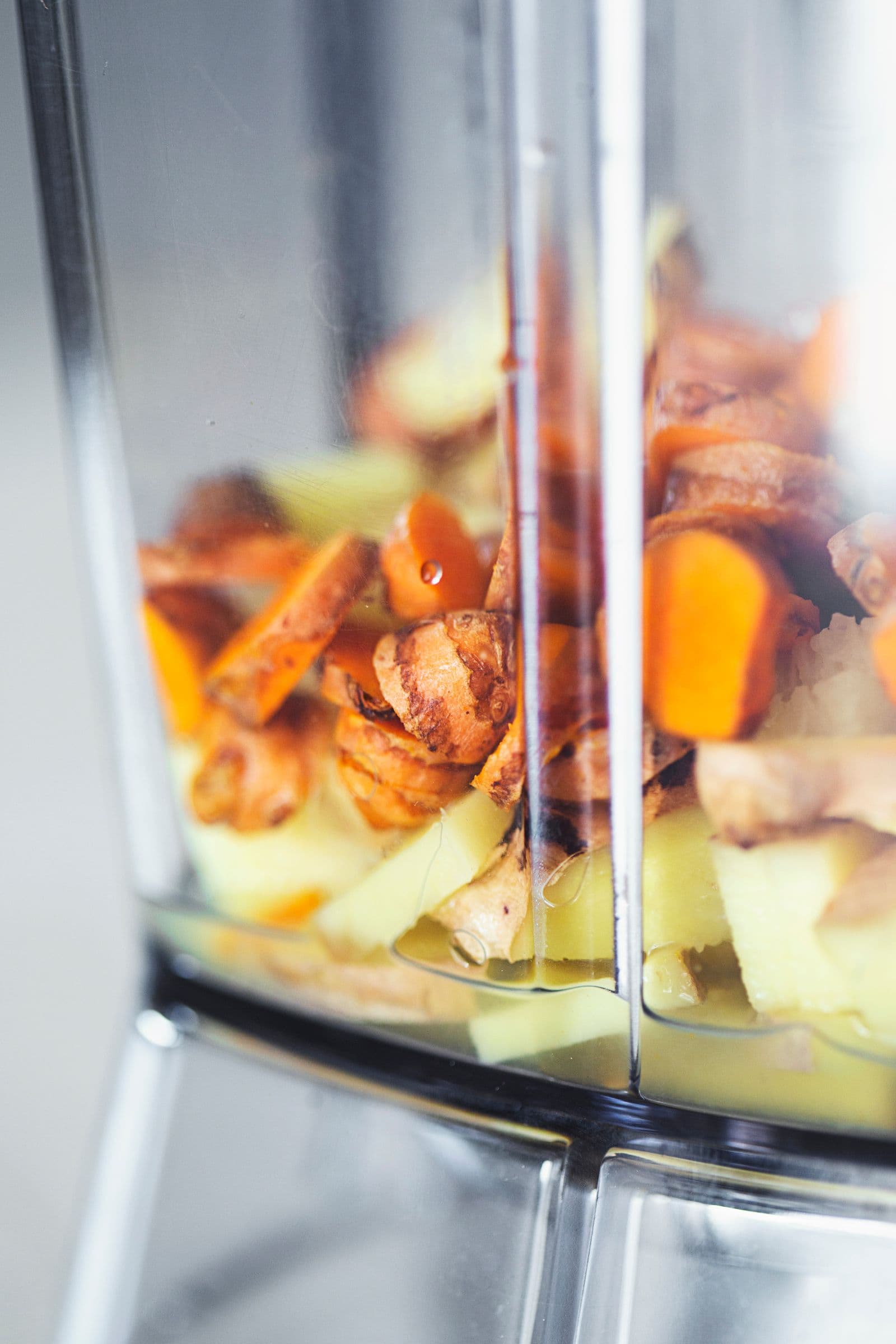 A blender jug filled with chunks of ginger, turmeric and lemon juice.