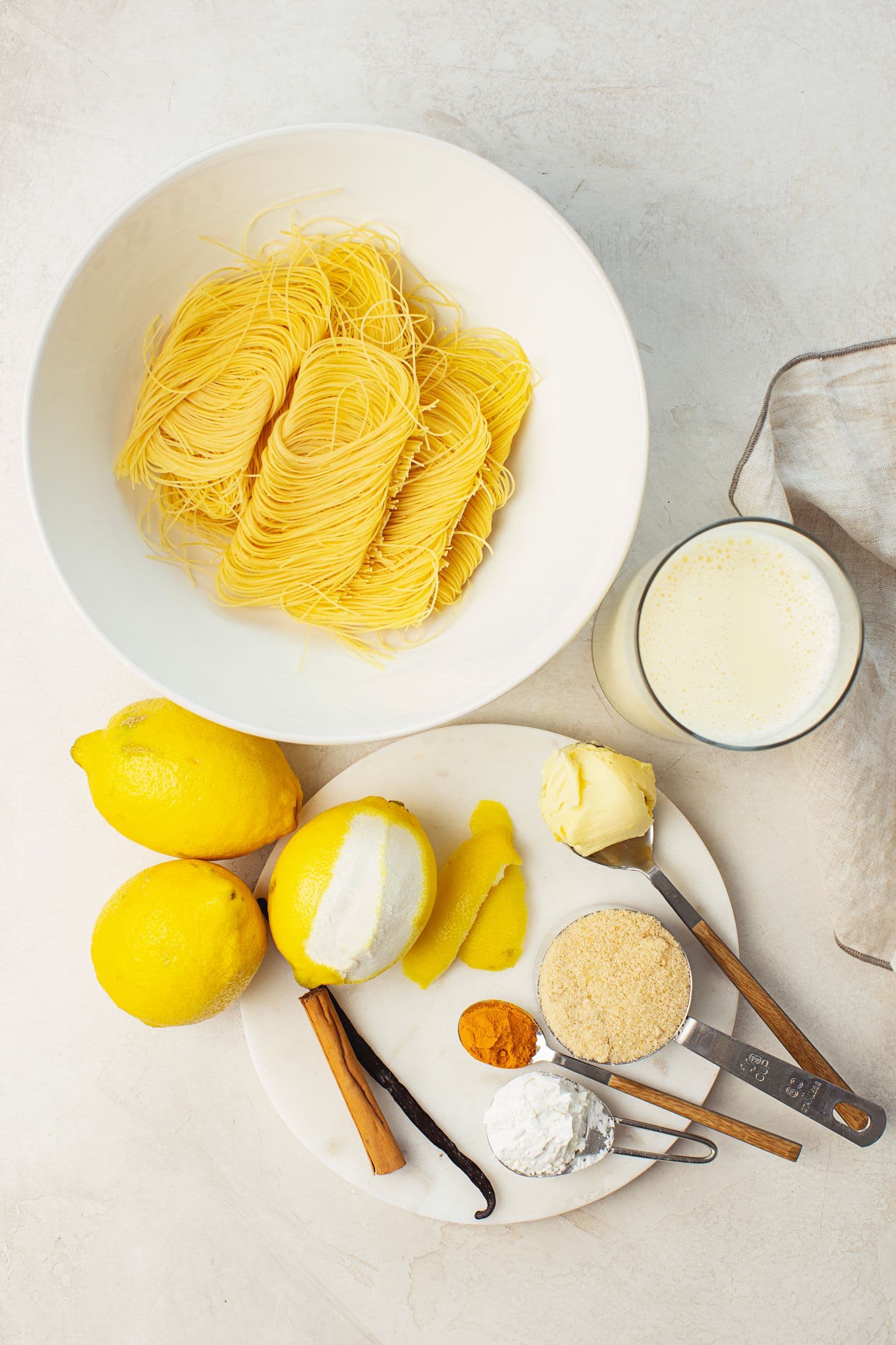 Overhead shot of ingredients for vegan Aletria: capellini nests, lemons, cinnamon stick, turmeric, sugar, vegan butter and soy milk.