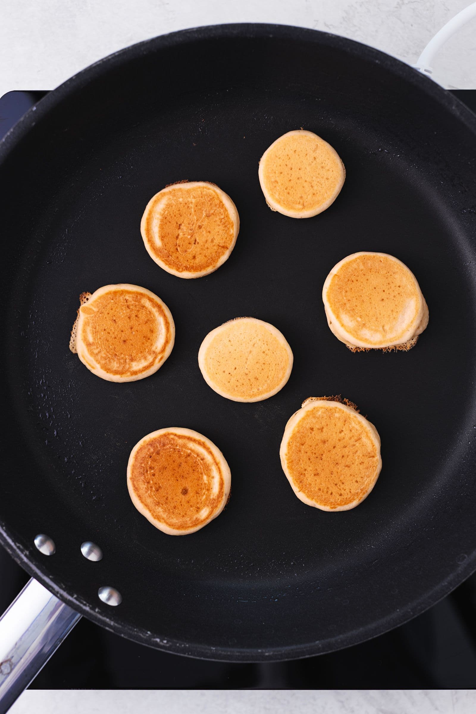 Mini vegan pancakes cooking on a non-stick frying pan, golden and fluffy on one side
