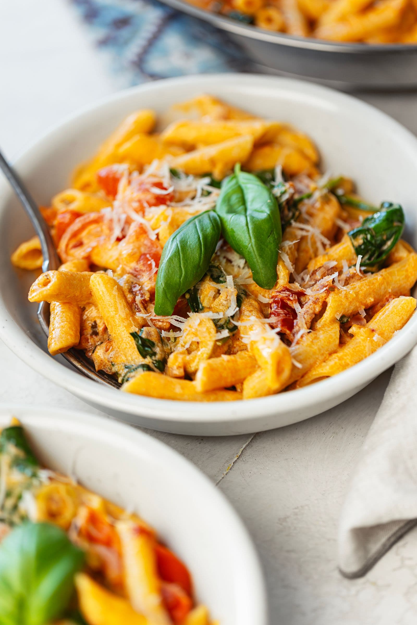 Side-angle shot of a bowl of creamy tomato and spinach penne with a fork and fresh basil