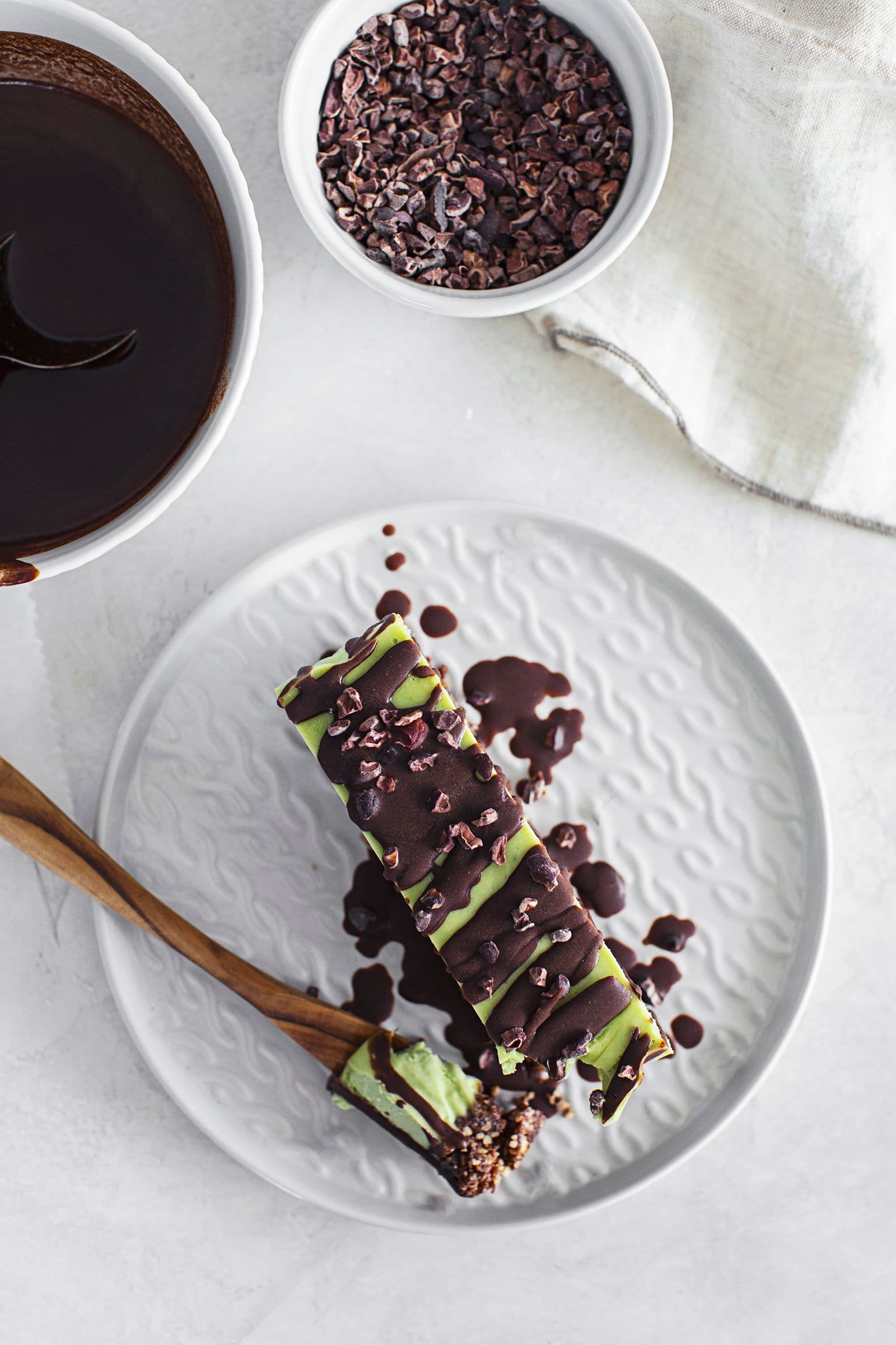 Slice of vegan mint and chocolate cheesecake with a nutty base, topped with melted chocolate and cacao nibs.