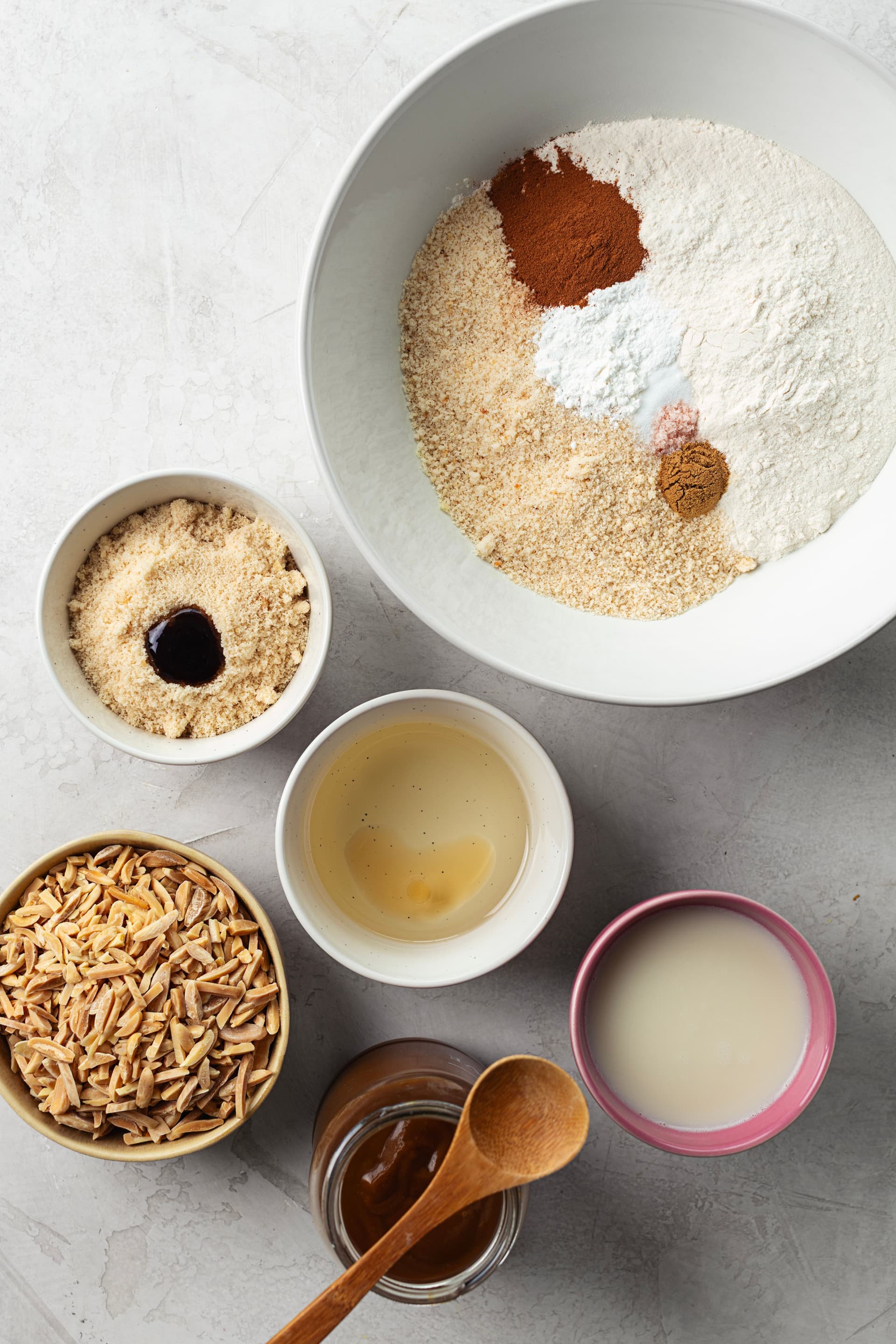 Ingredients for a vegan almond cake: flour, spices, brown sugar, slivered almonds, coconut caramel and plant milk.