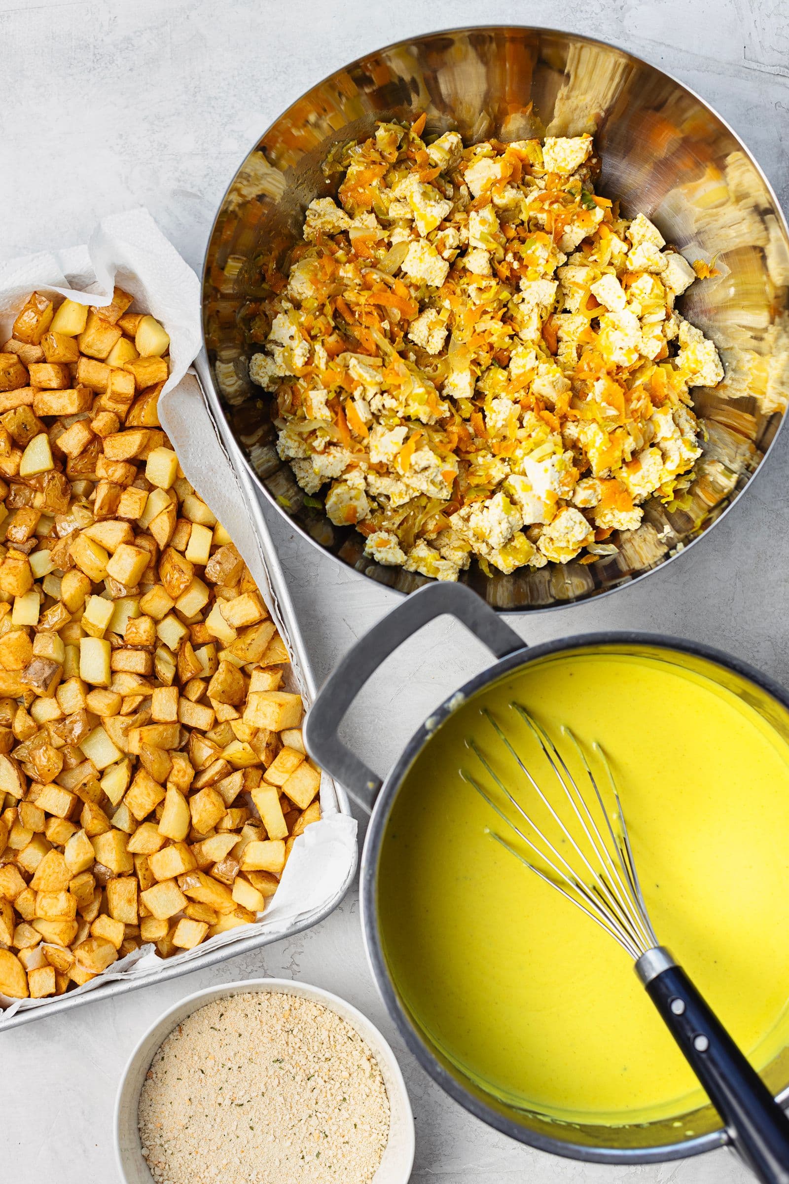 Tofu and vegetable sauté in a bowl, golden fried potatoes and the béchamel sauce ready to assemble.