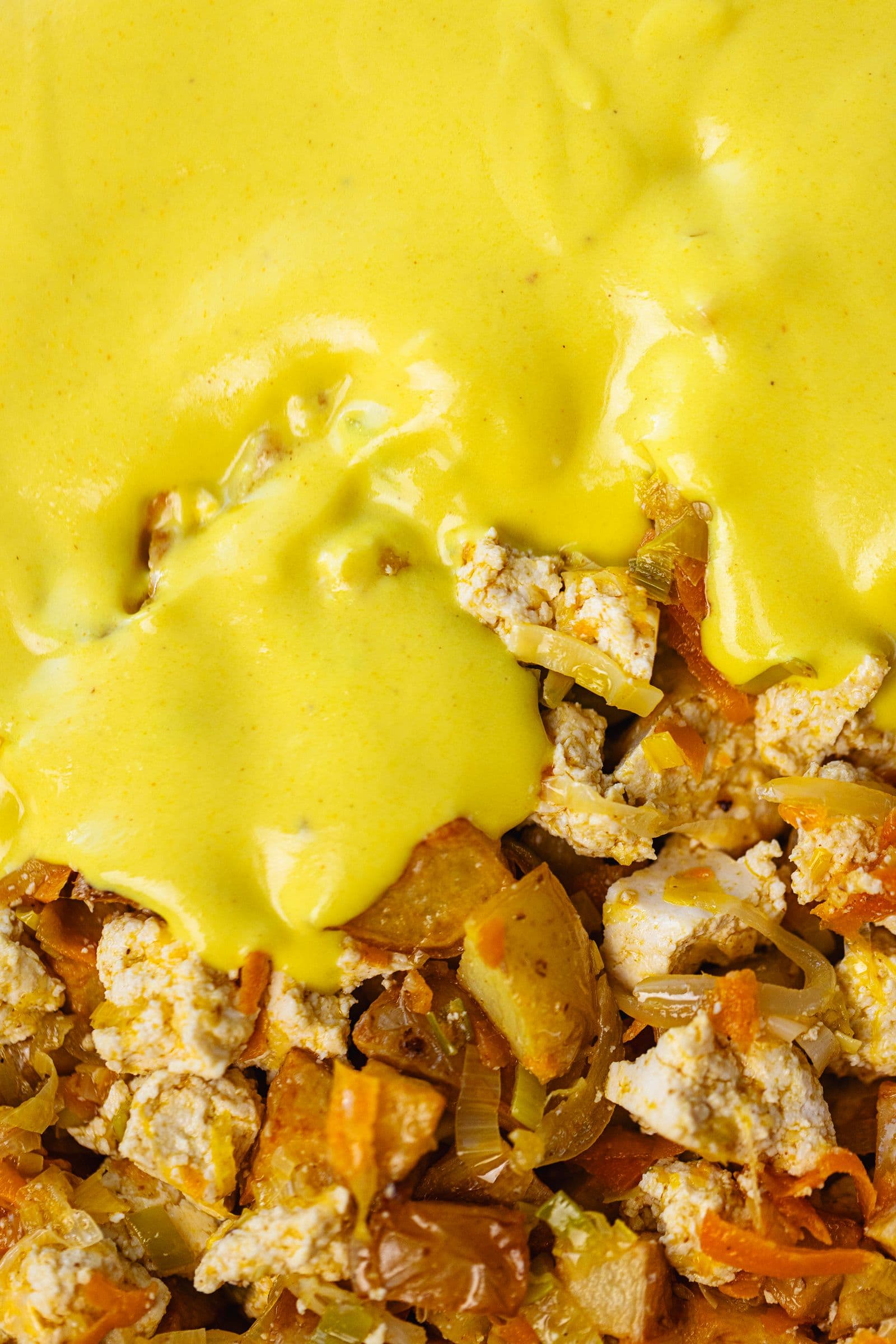 Close-up of creamy béchamel spreading over the tofu, potatoes and vegetables.