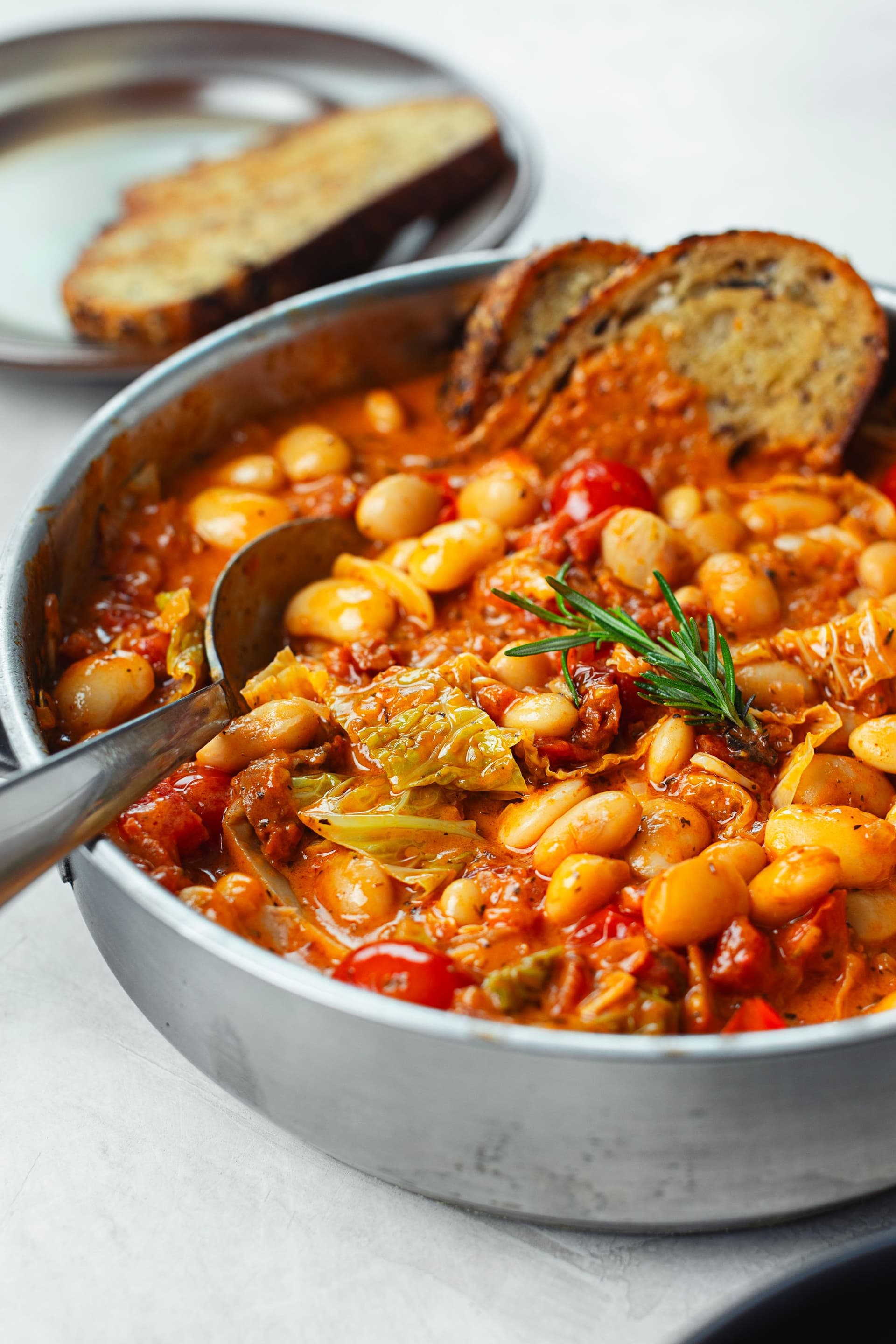 Side angle of the pot filled with the creamy tomato-coconut bean stew, with toasted bread tucked inside.