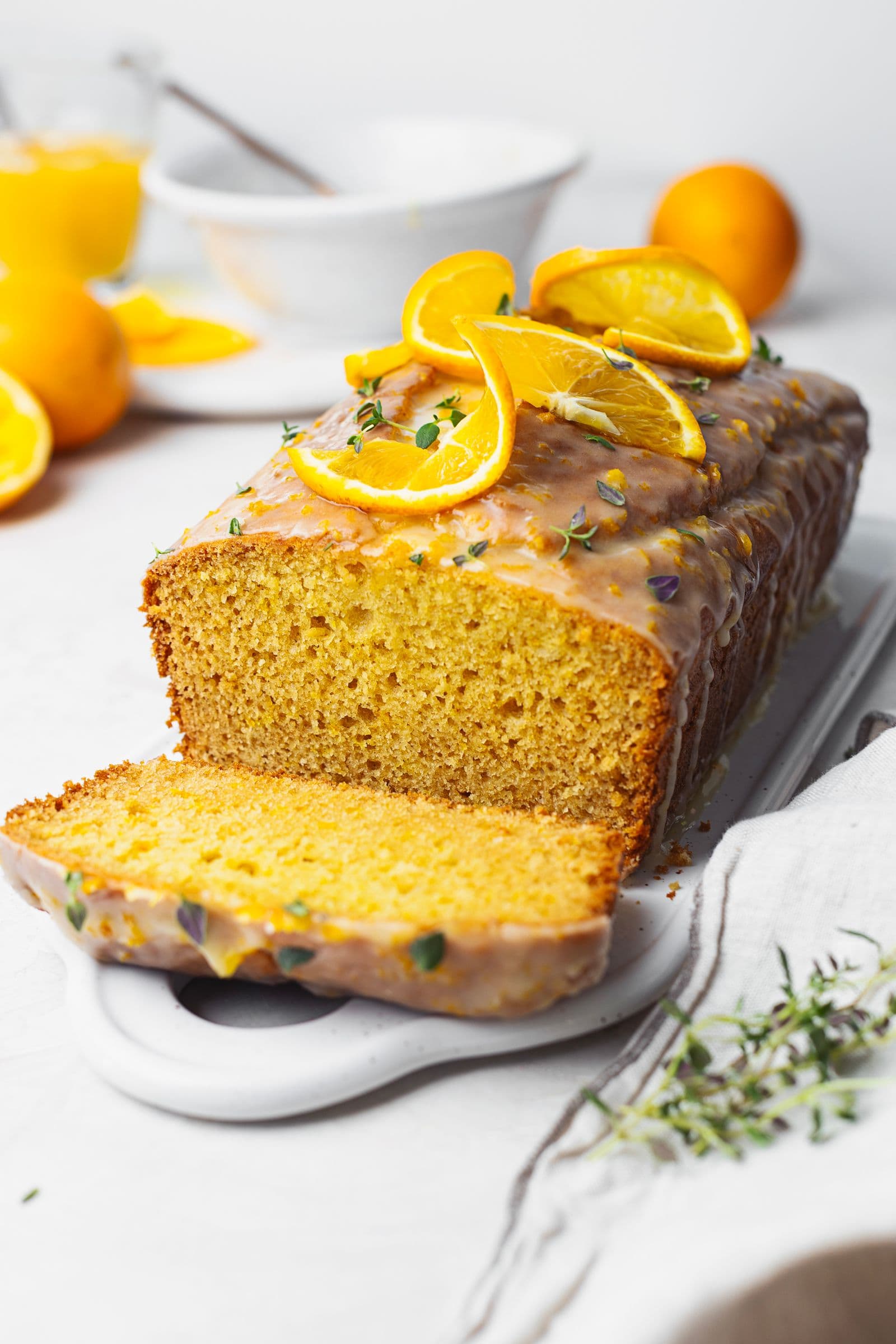 Moist orange cake with orange glaze, topped with fresh orange slices and thyme, served on a white platter.
