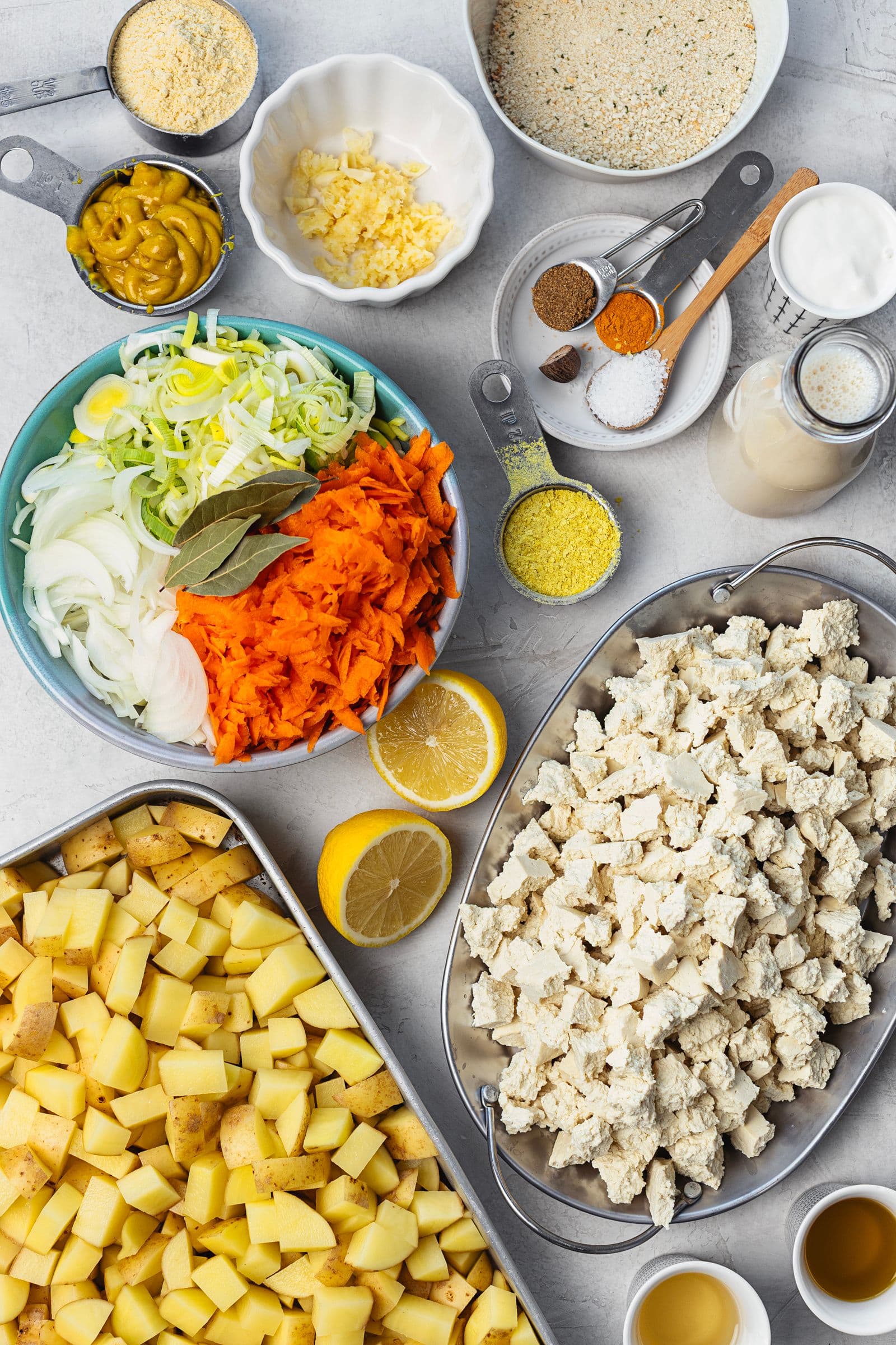 Ingredients prepped for the gratin: tofu pieces, potatoes, sliced vegetables and béchamel components arranged in bowls.