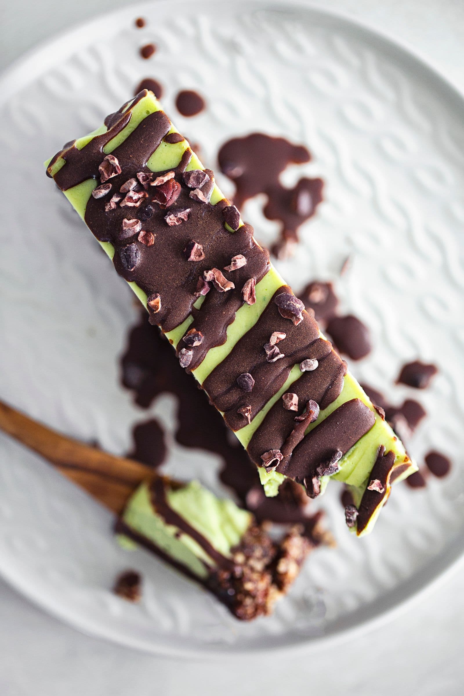 Close-up of slice of vegan mint and chocolate cheesecake with a nutty base, topped with melted chocolate and cacao nibs.