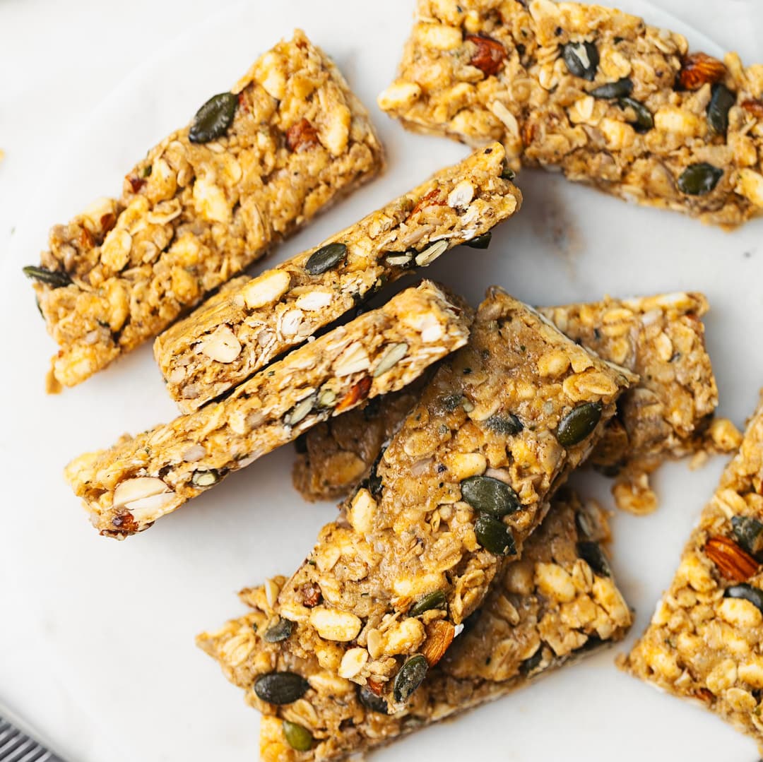 Homemade protein bars with oats, seeds, nuts and tahini, cut into rectangles and stacked on a marble plate.