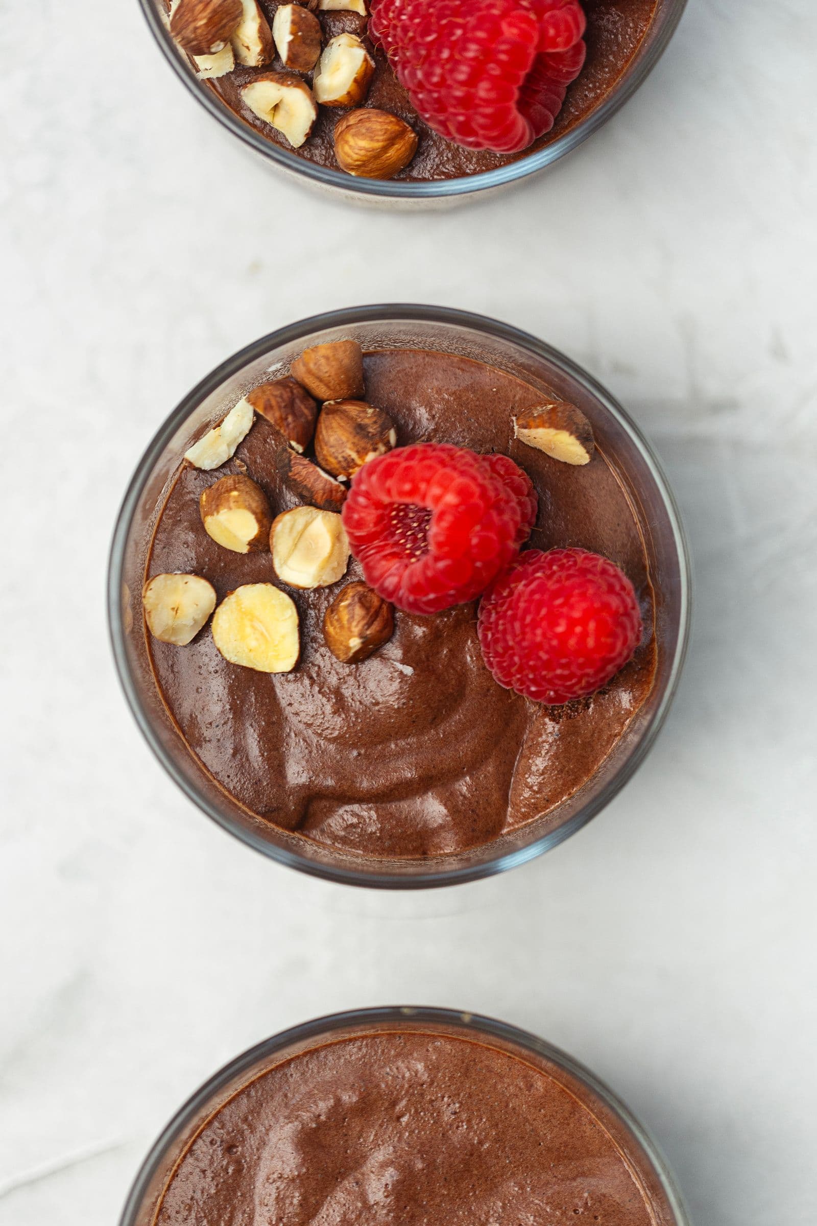 Vegan chocolate mousse topped with fresh raspberries and toasted hazelnuts.