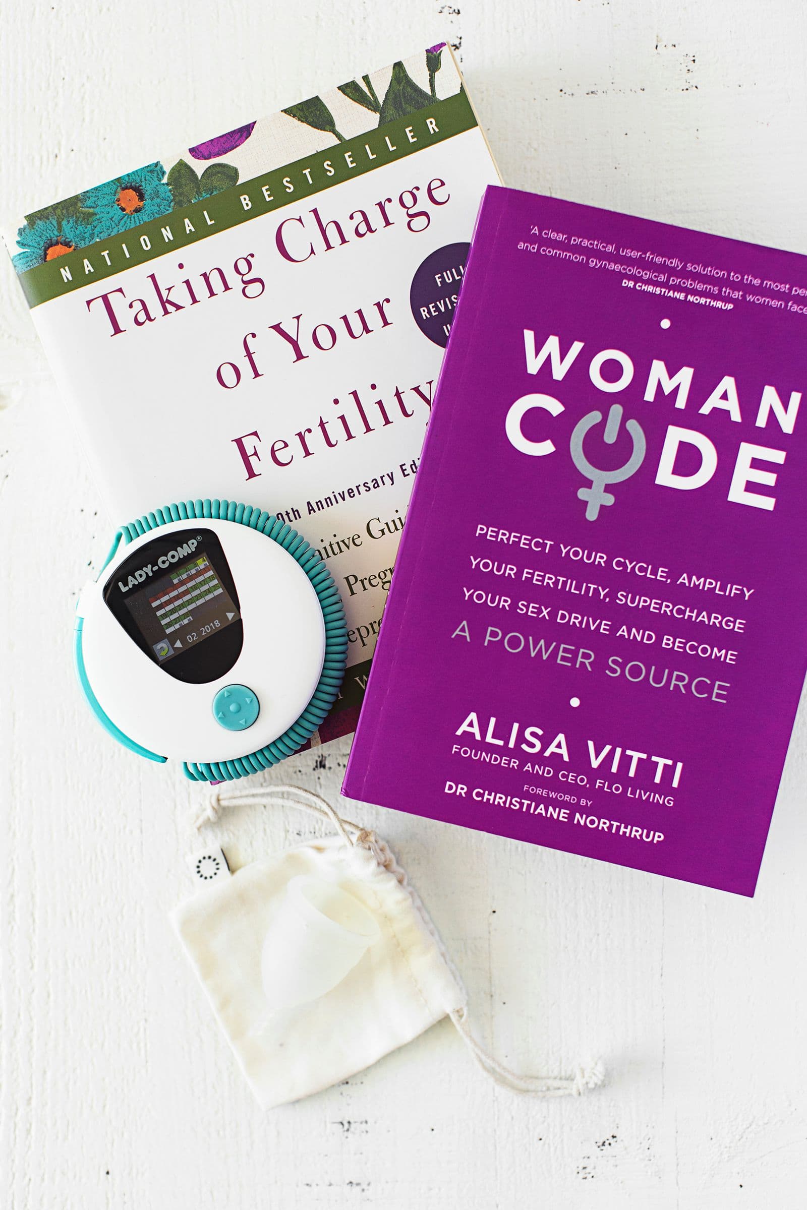 Basal temperature thermometer and books related to hormone balance placed on a white surface.