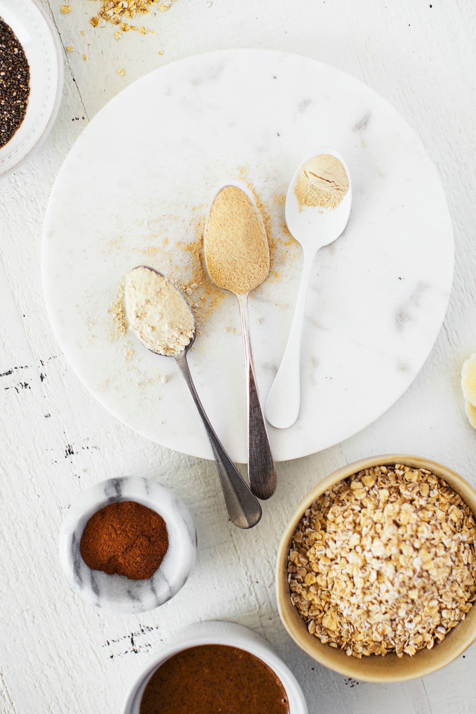 Three spoons with different adaptogenic powders on a plate surrounded by oats and spices.