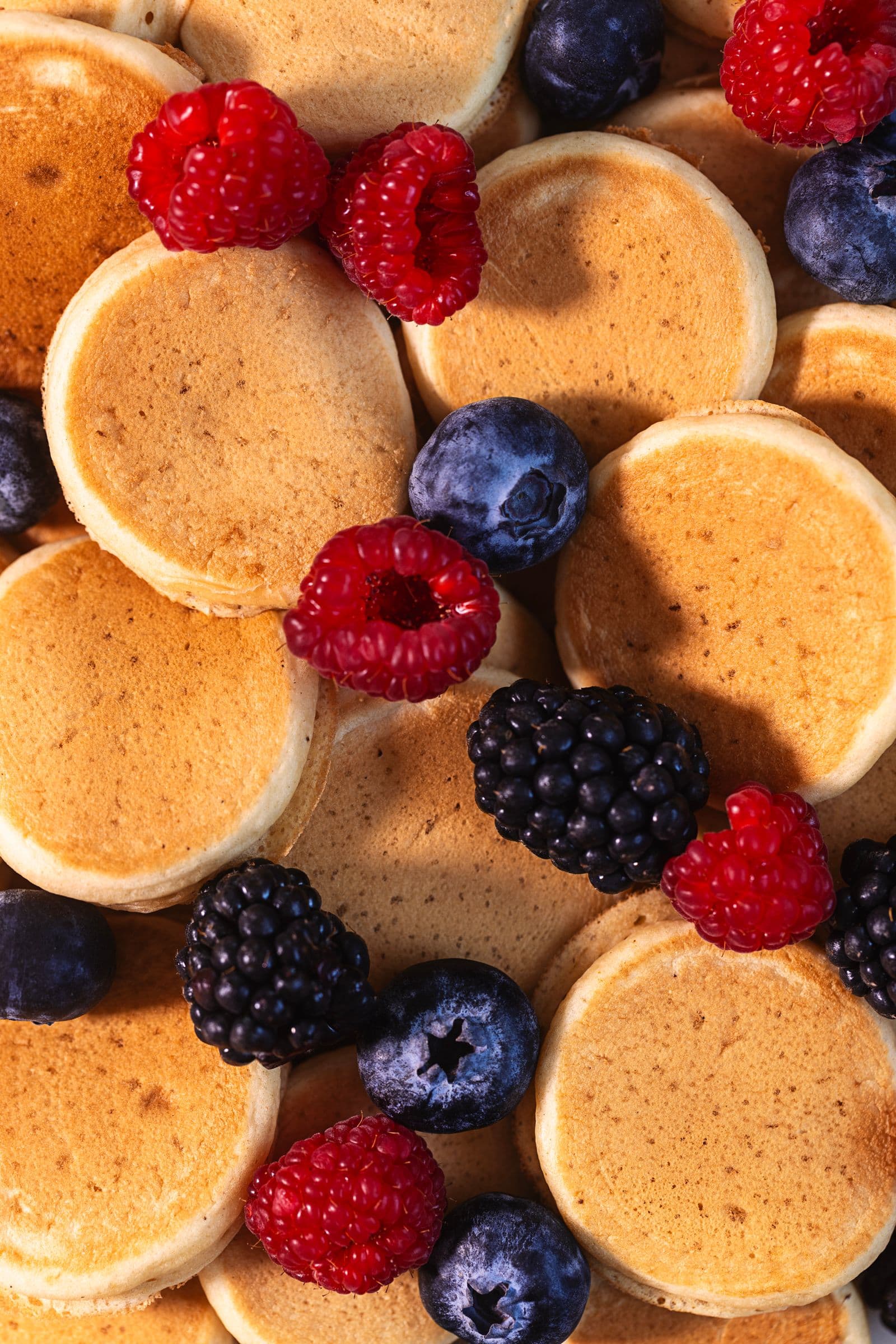 Close-up of golden mini vegan pancakes topped with fresh raspberries, blueberries, and blackberries