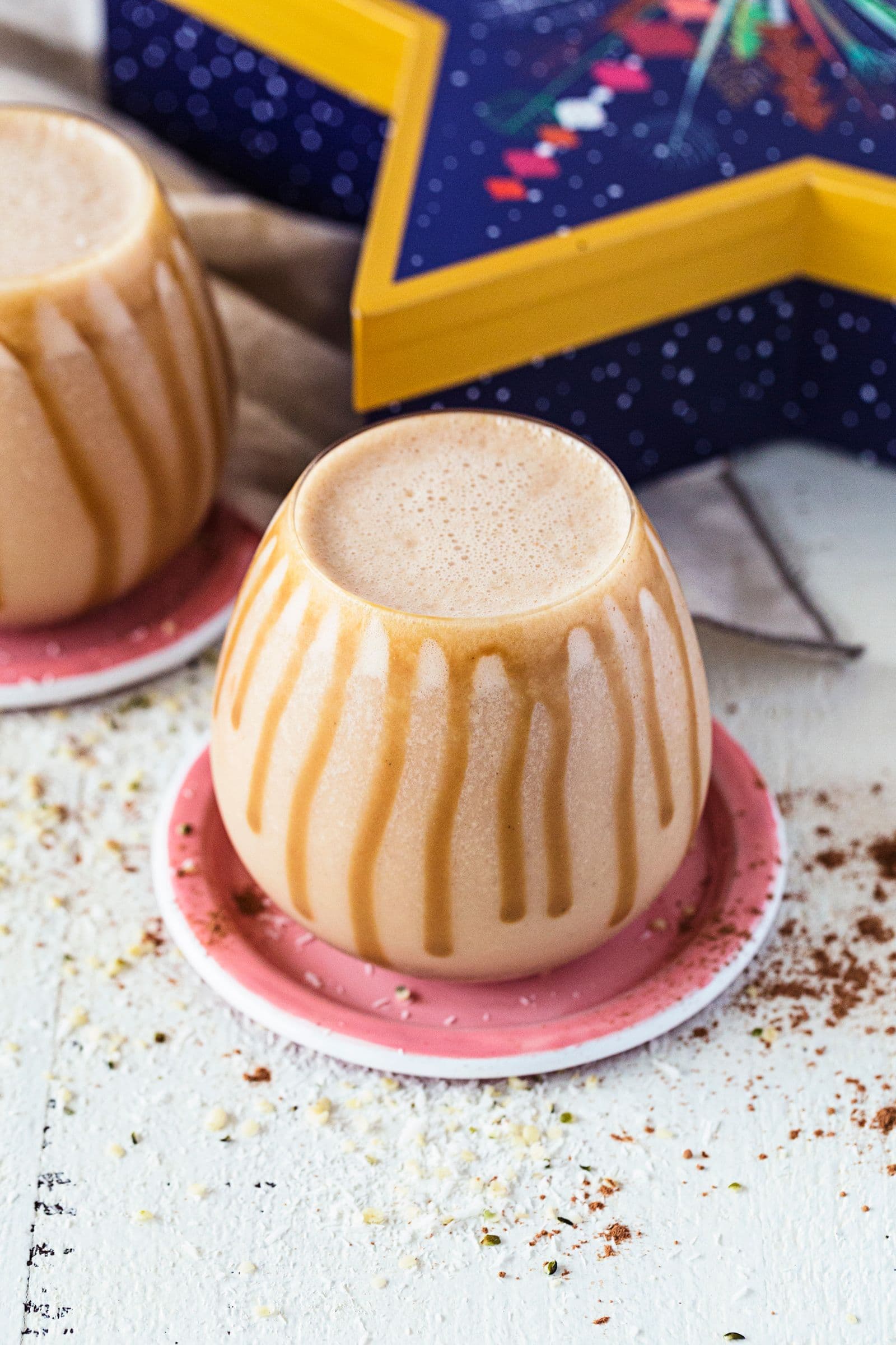 Copo arredondado com smoothie de caramelo salgado e manteiga de amendoim, servido em base cor-de-rosa, com fio de caramelo escorrido pelas laterais.