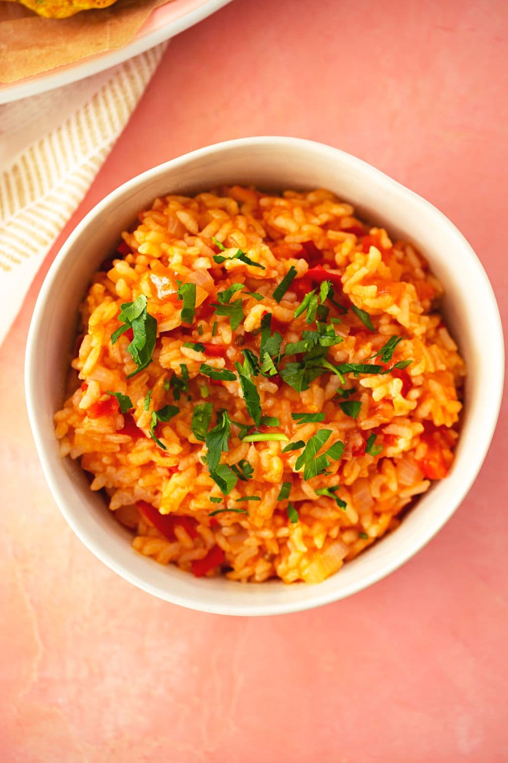 White bowl of tomato rice with bell peppers, topped with fresh parsley