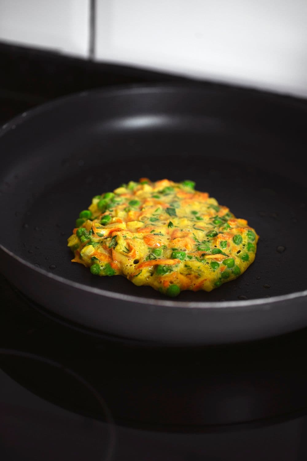 Chickpea and veggie fritter cooking in a non-stick skillet