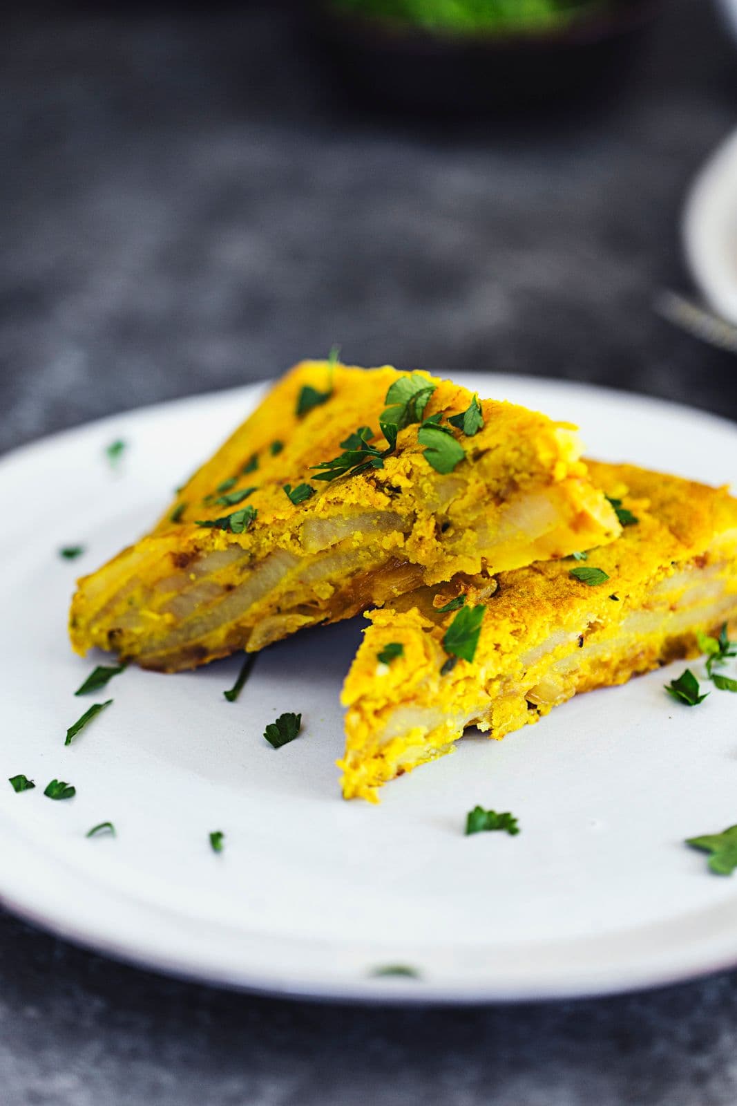 Triangular slices of vegan Spanish tortilla on a white plate, sprinkled with parsley.