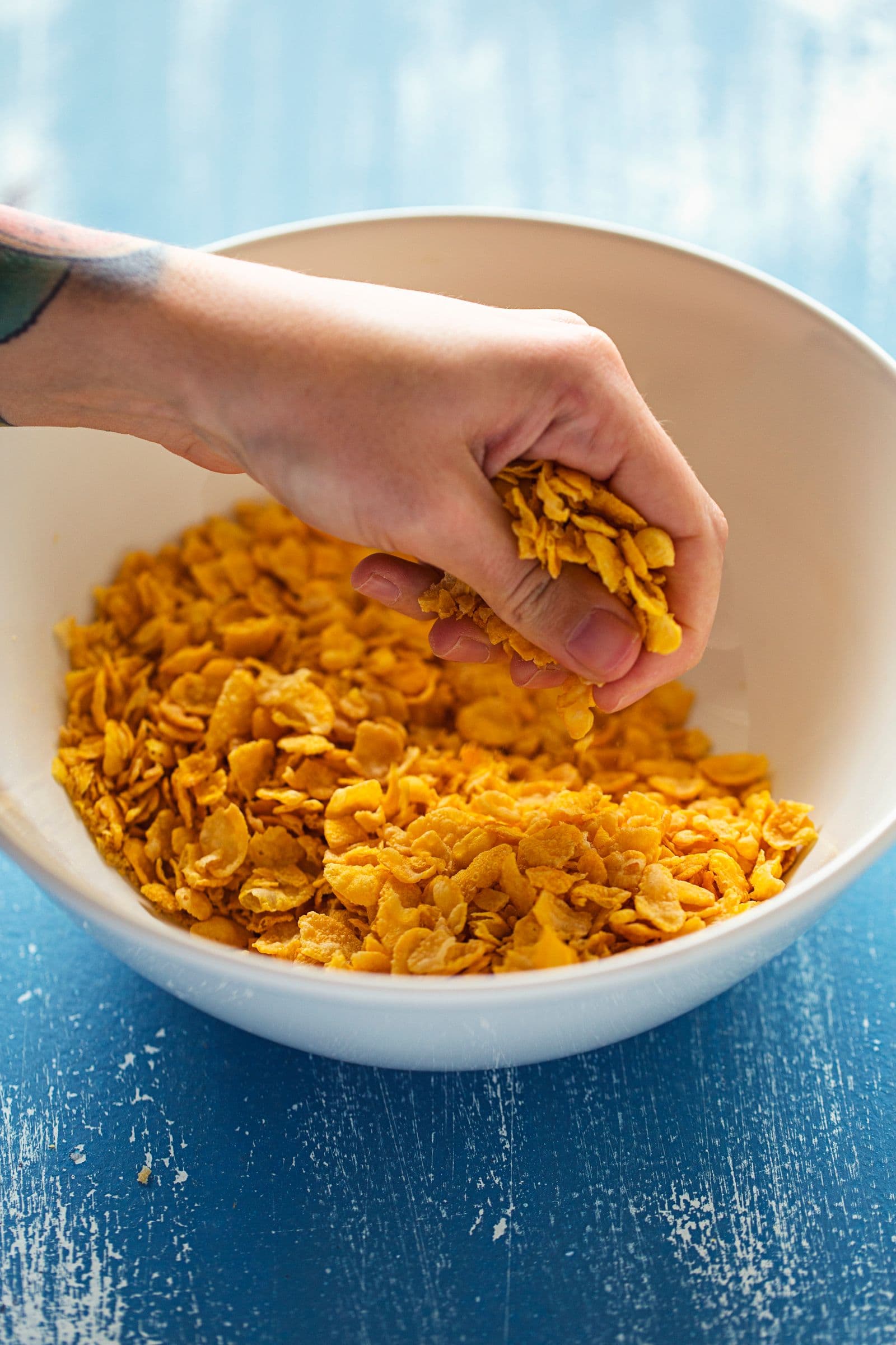 Hand crunching cornflakes in a mixing bowl for the granola base.