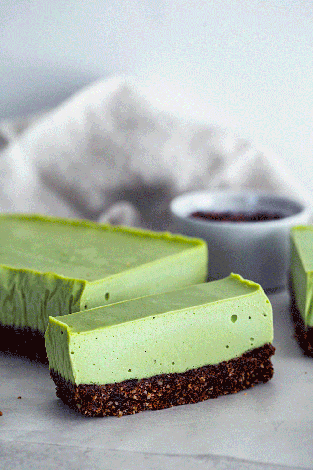 Animated gif of hand drizzling melted chocolate and sprinkling cacao nibs over a slice of vegan mint cheesecake.