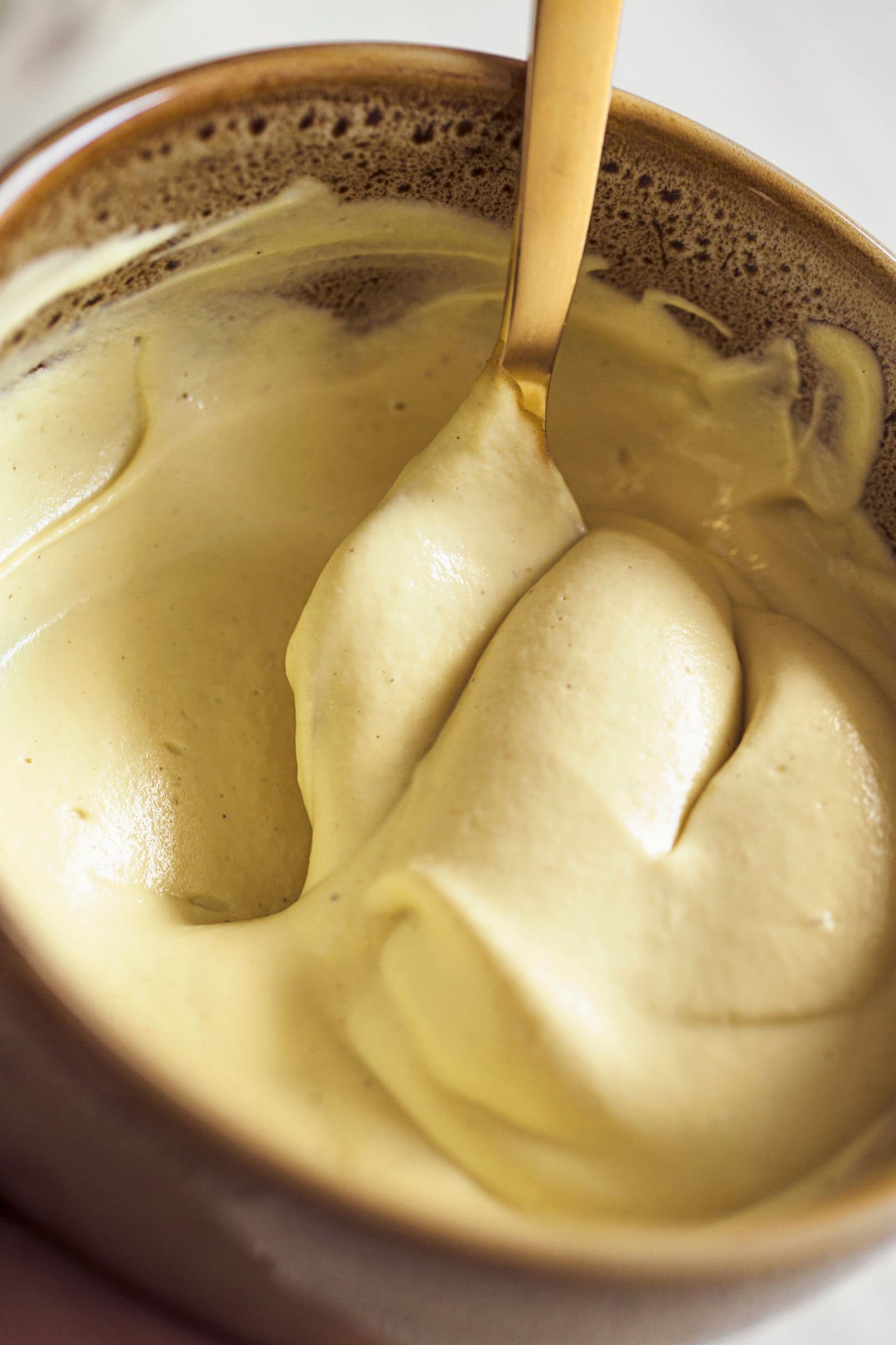 Creamy vegan mango yogurt mixture being stirred with a golden spoon.
