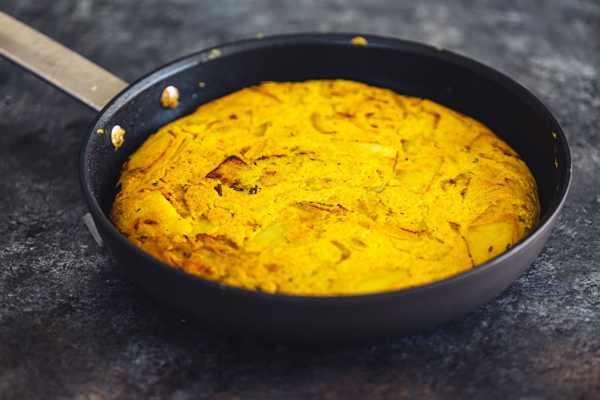 Cooked vegan Spanish tortilla cooking in a black skillet.