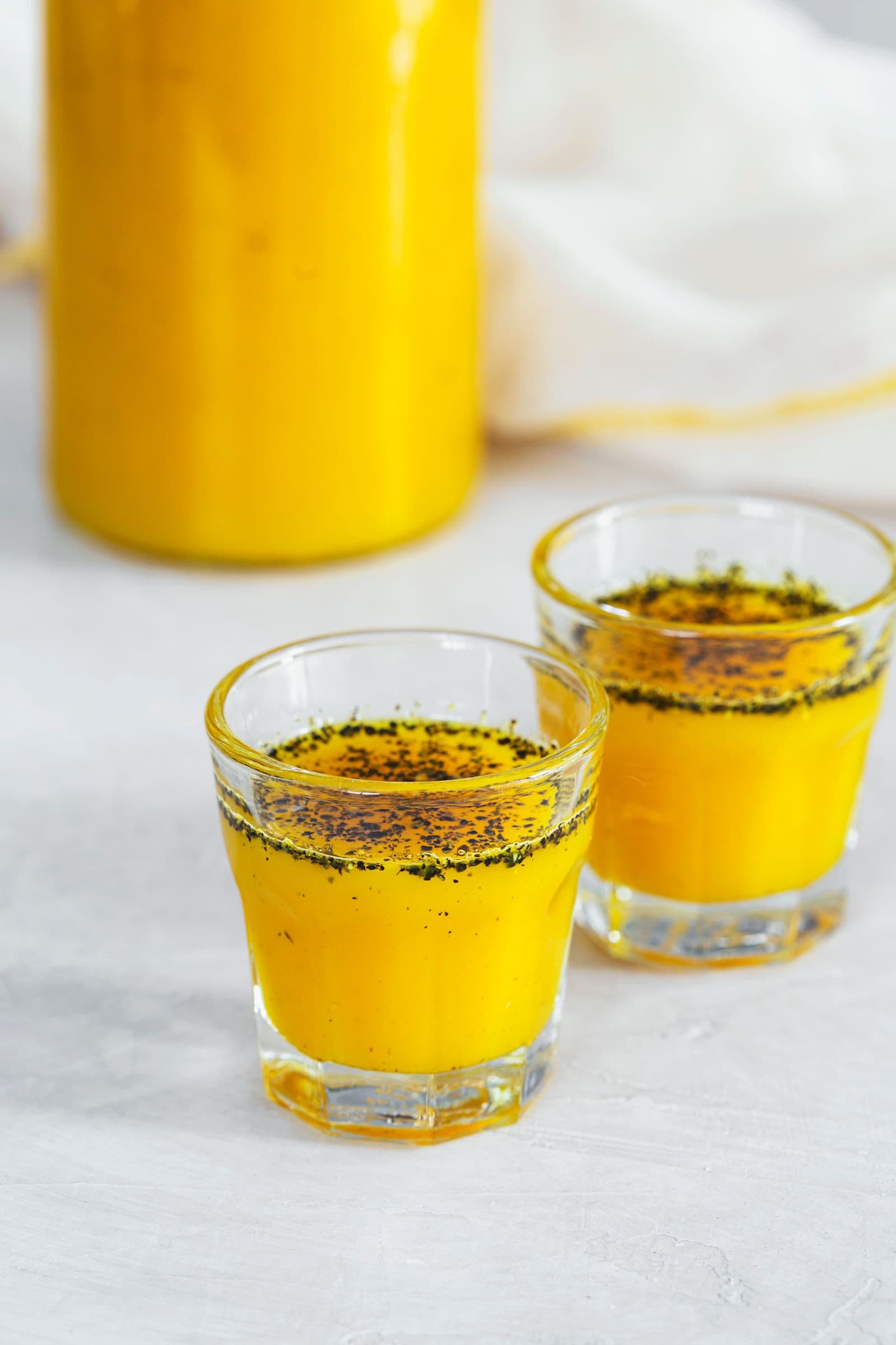 A glass bottle and two shot glasses filled with ginger turmeric syrup.