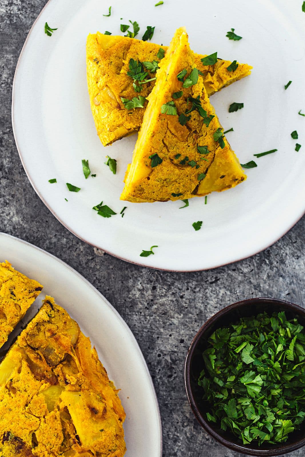 Two slices of vegan Spanish tortilla arranged on a white plate, topped with parsley.