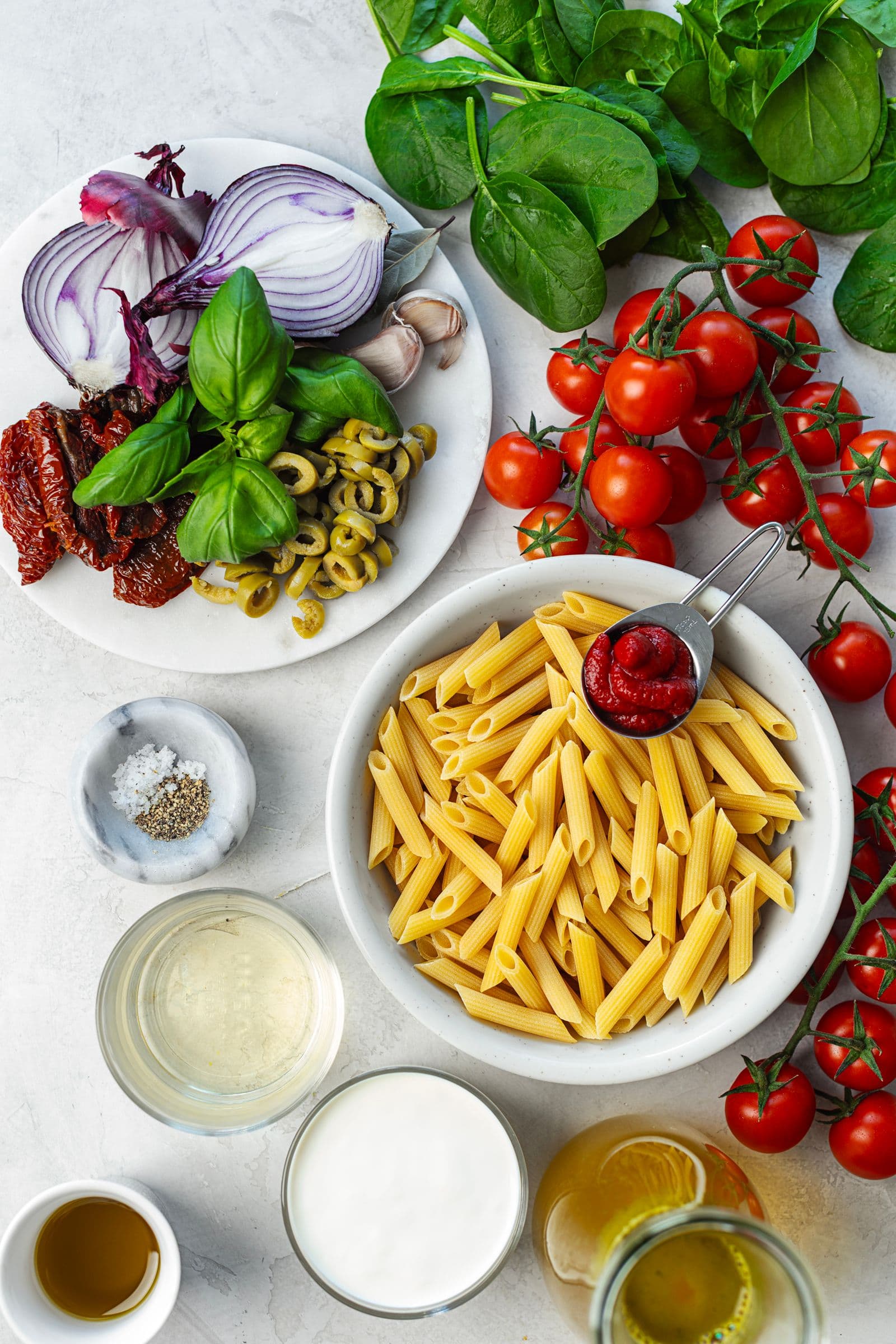 Flat lay of ingredients for creamy tomato and spinach penne, including cherry tomatoes, spinach, olives and soy cream