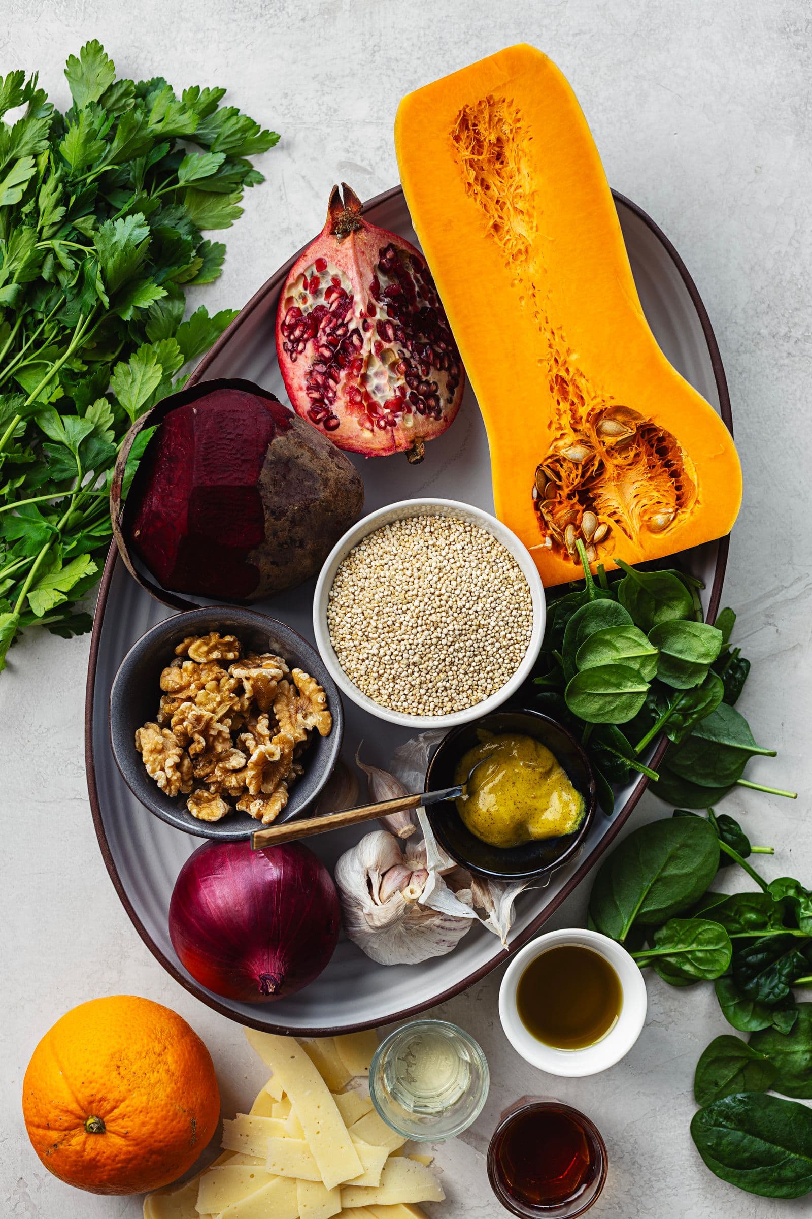 Ingredients for a winter quinoa salad with butternut squash, beetroot, spinach, pomegranate, walnuts and citrus vinaigrette, arranged on a platter.