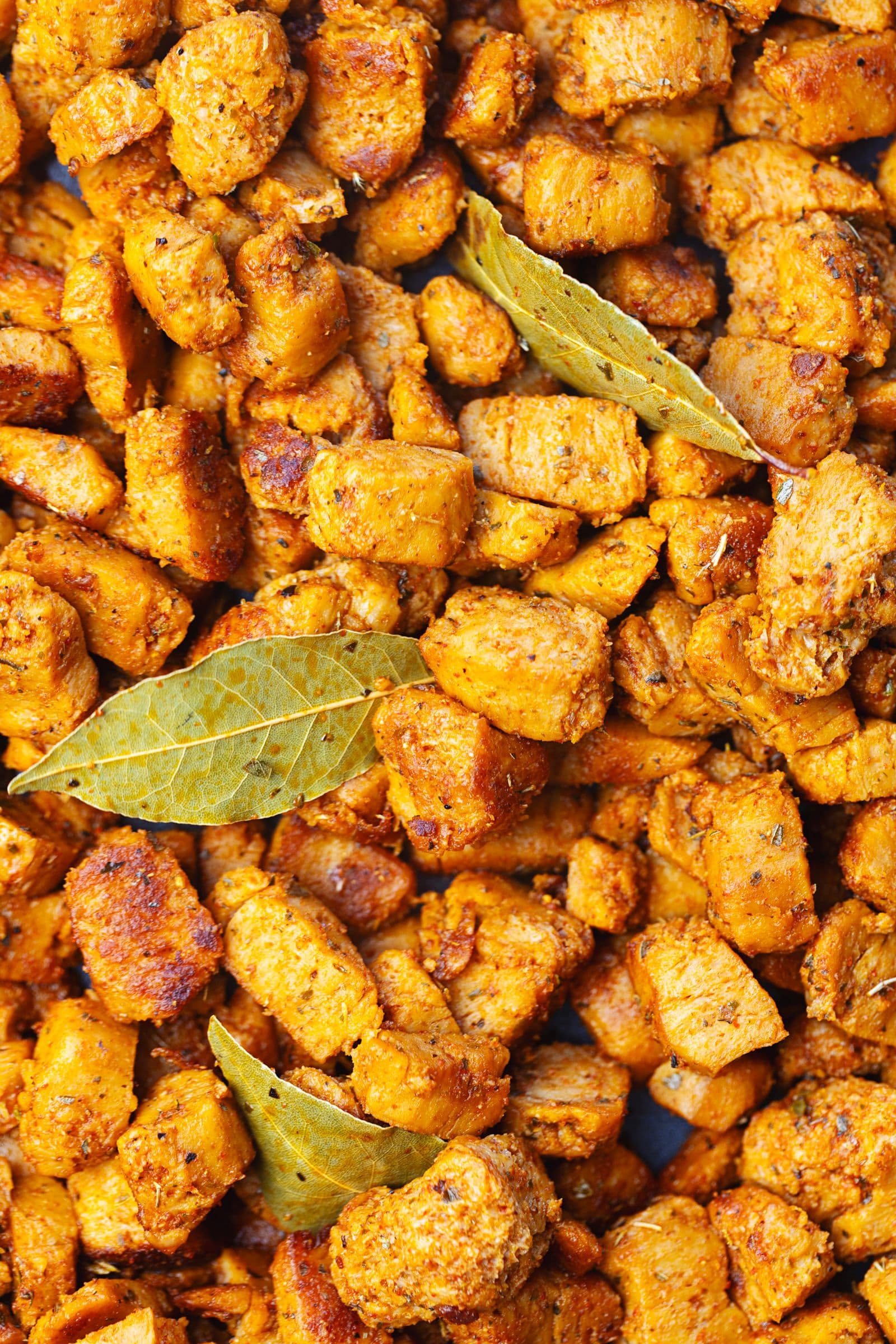 Close-up of caramelised spiced soy chunks with bay leaves in a dark pan