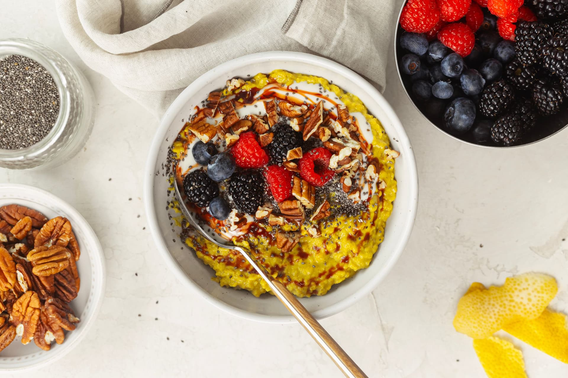 Golden oatmeal with chia, pecans, berries, plant yogurt and date syrup, served in a white bowl with a spoon