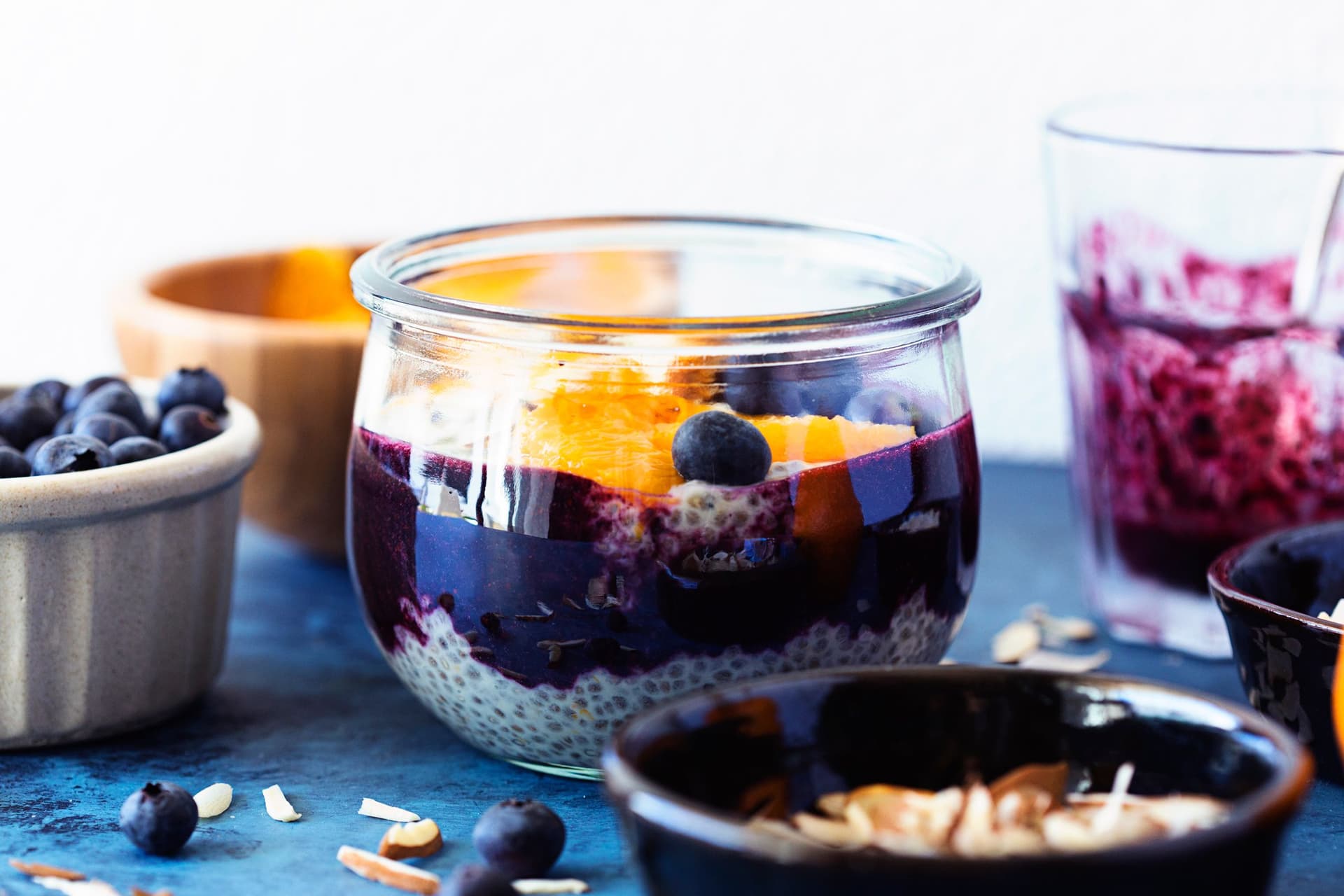 Glass jar showing layers of chia pudding, blueberry purée and orange slices.