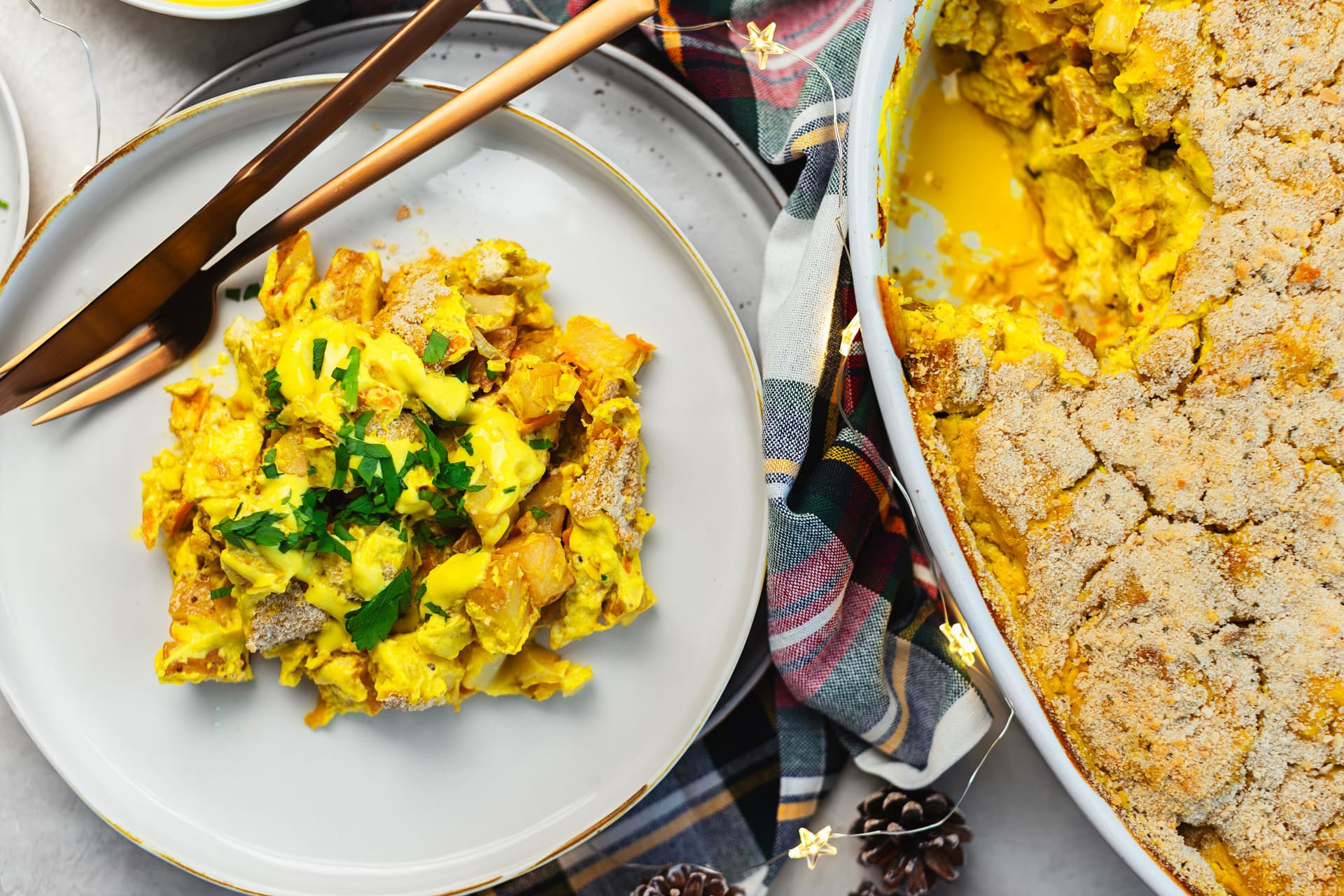 Top view of a plated serving of the gratin, utensils and white casserole dish beside it..