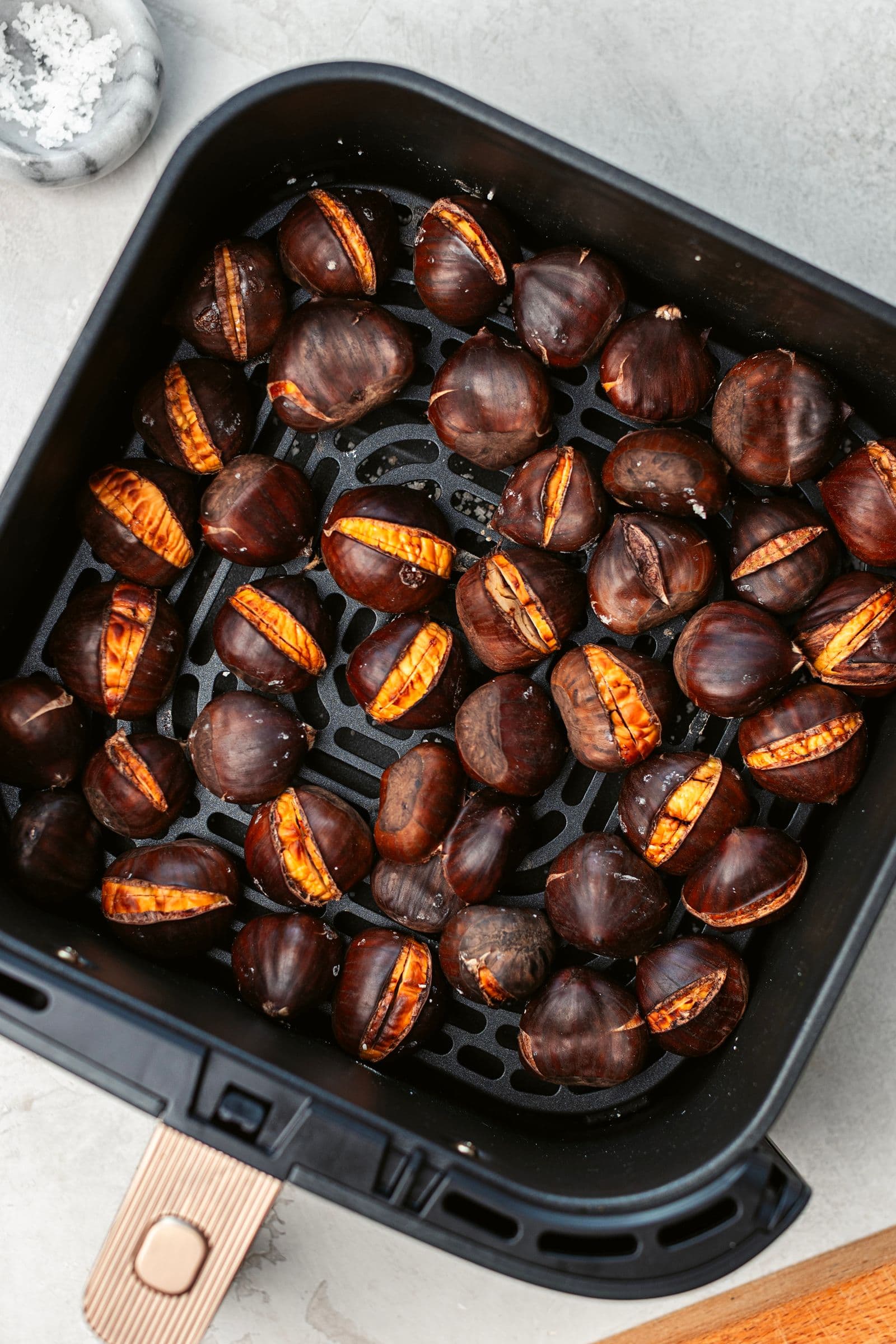 Roasted chestnuts inside the air fryer basket, with the shells opening along the scored lines.”
