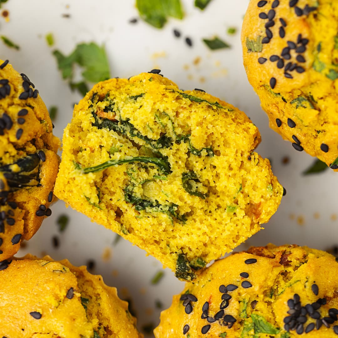 Savoury chickpea muffin with spinach and tomatoes, sliced to reveal the fluffy inside.