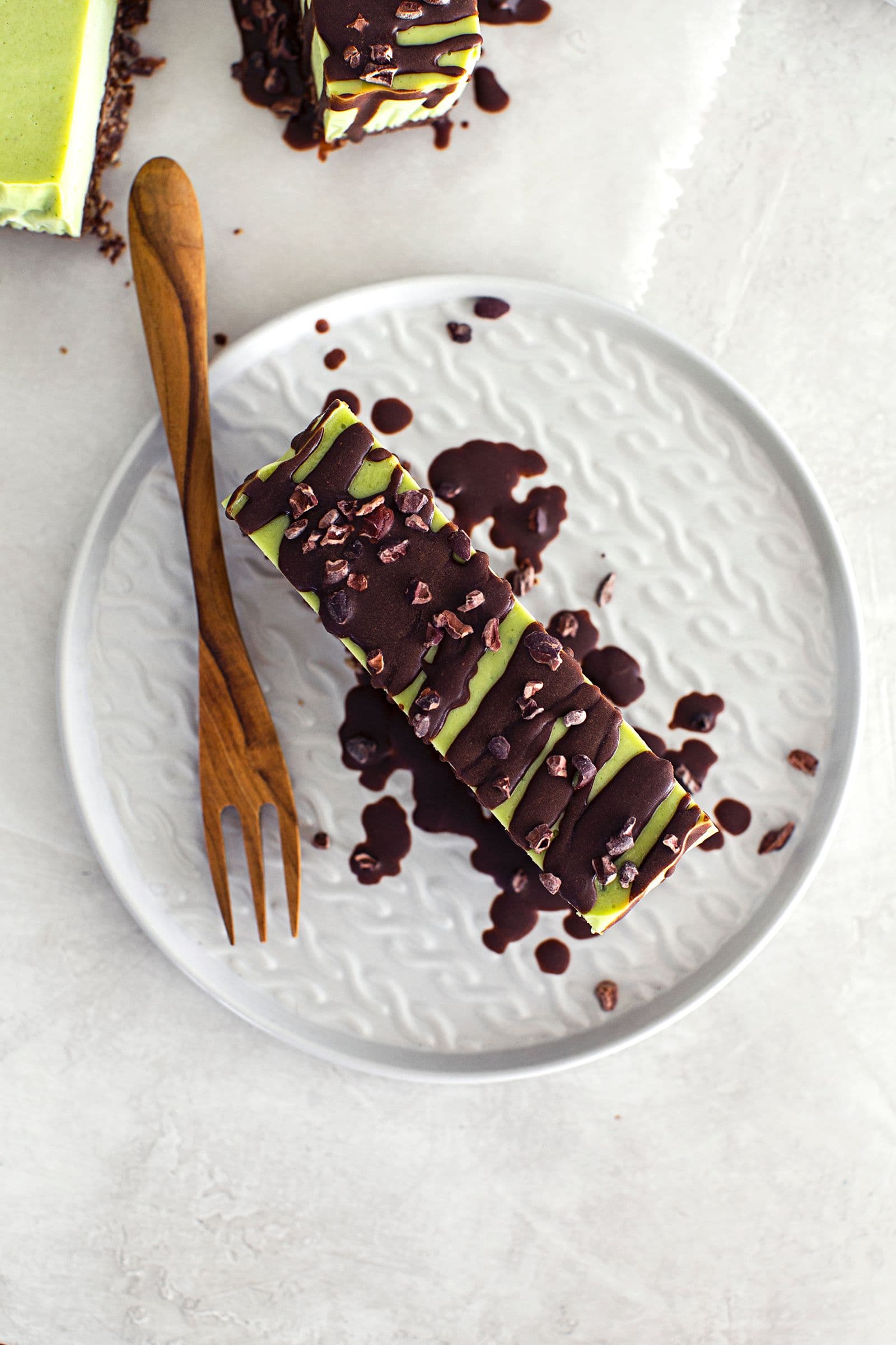 Slice of vegan mint and chocolate cheesecake with a nutty base, topped with melted chocolate and cacao nibs.