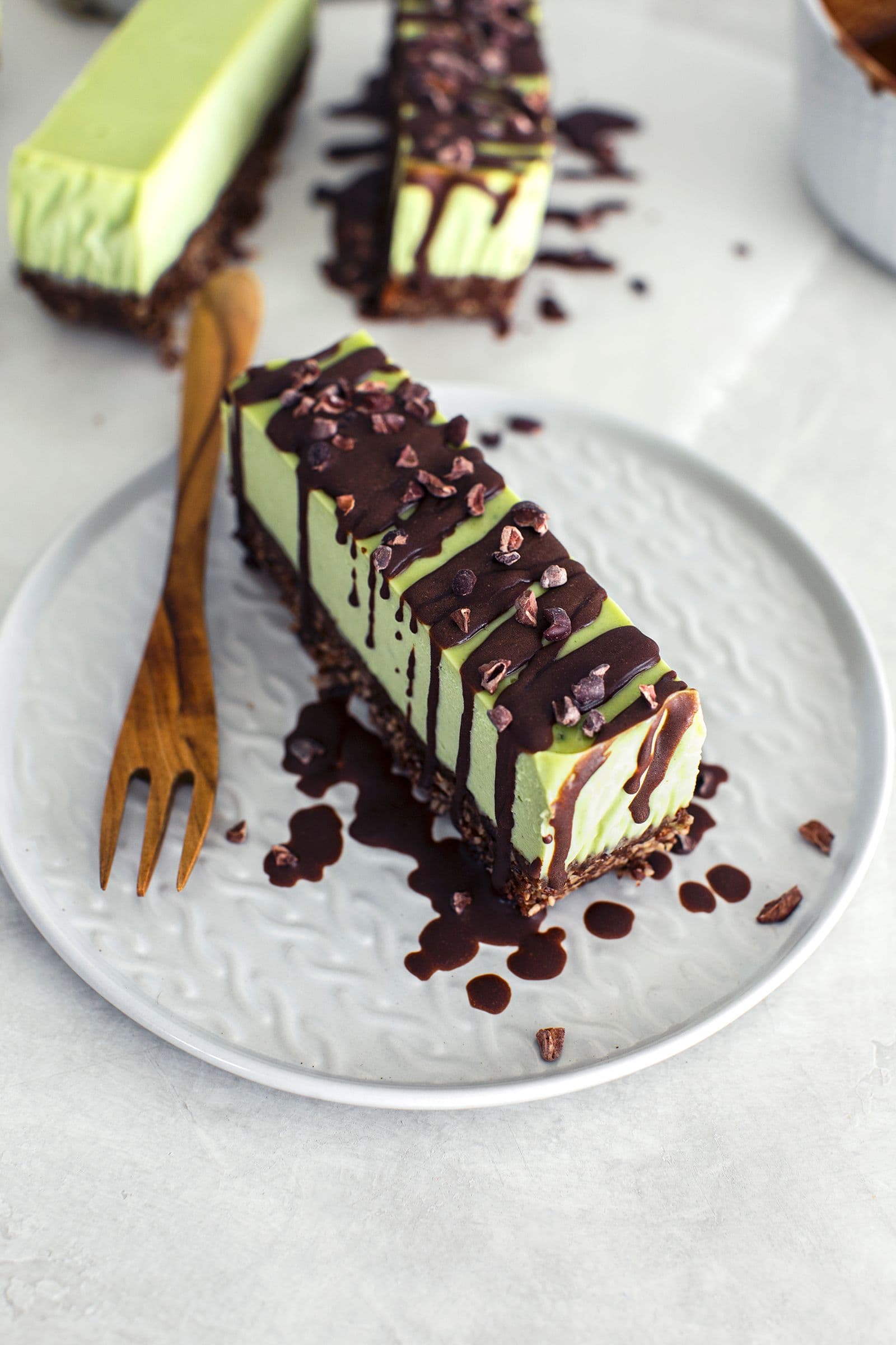 Slice of vegan mint and chocolate cheesecake with a nutty base, topped with melted chocolate and cacao nibs.