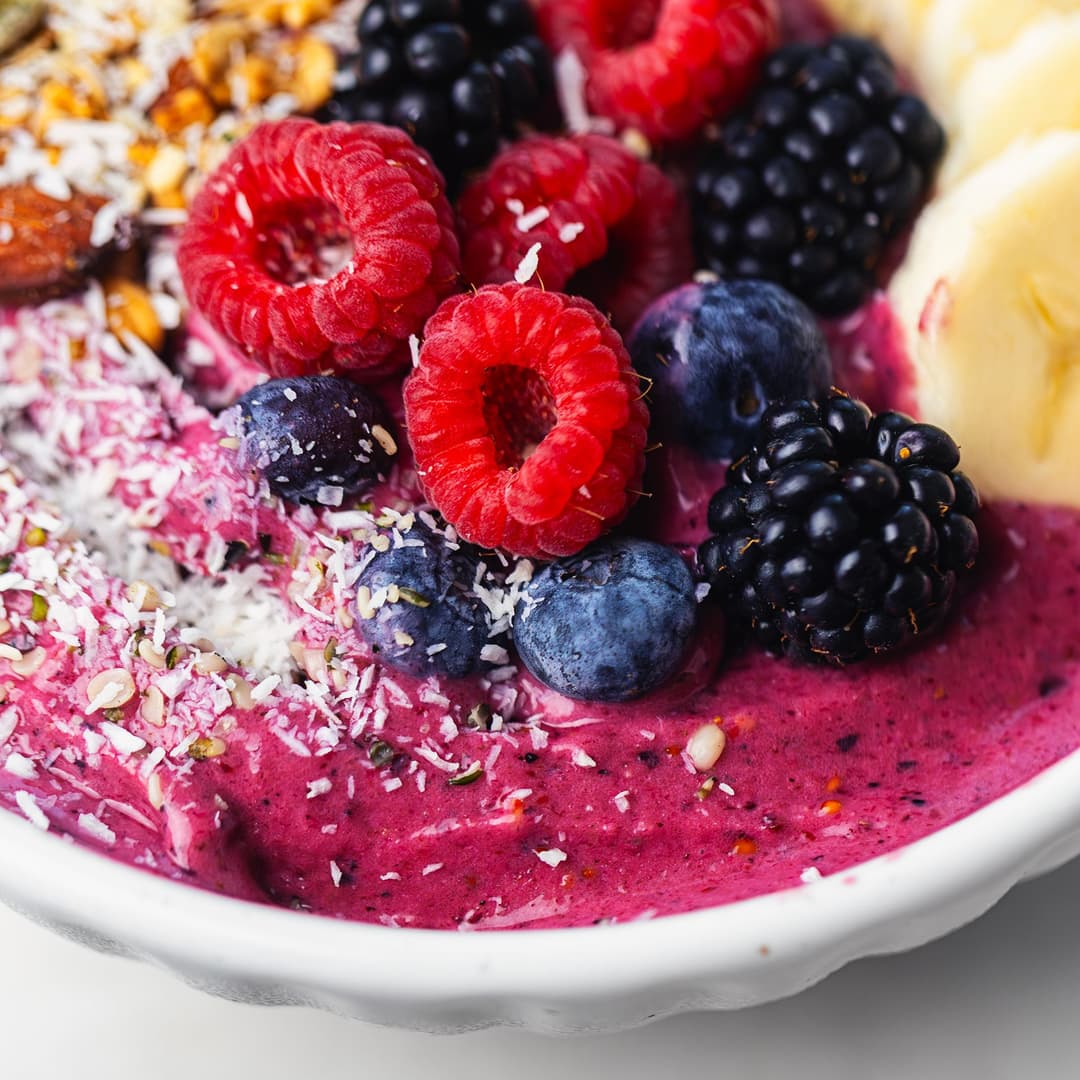 Berry smoothie bowl topped with banana, raspberries, blackberries, blueberries, coconut and granola.