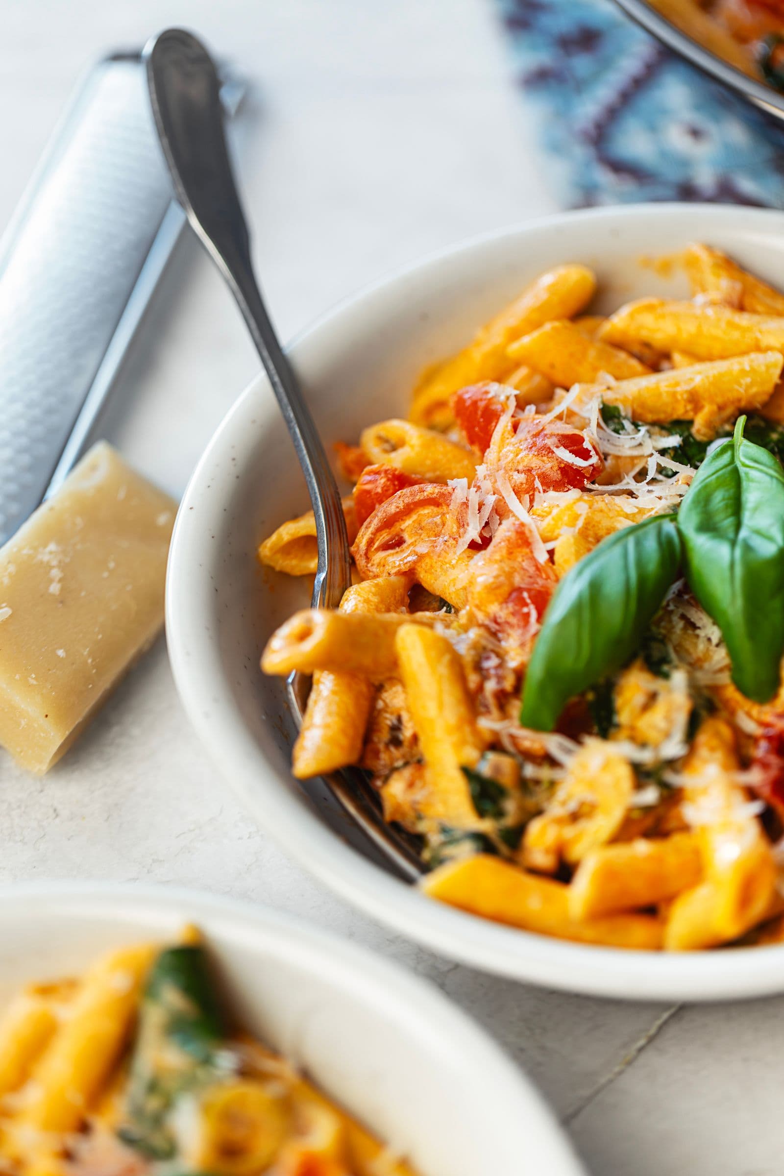 Close-up of creamy tomato and spinach penne with a fork, topped with grated vegan parmesan and fresh basil