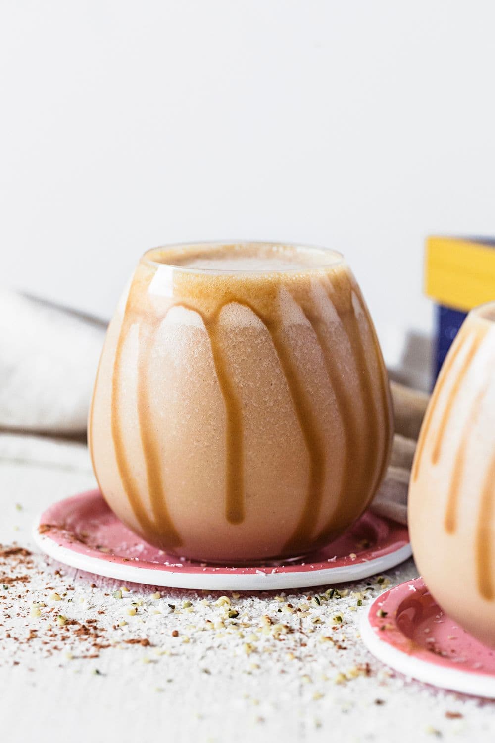 Rounded glass with salted caramel and peanut butter smoothie, drizzled with caramel sauce, on a pink coaster.