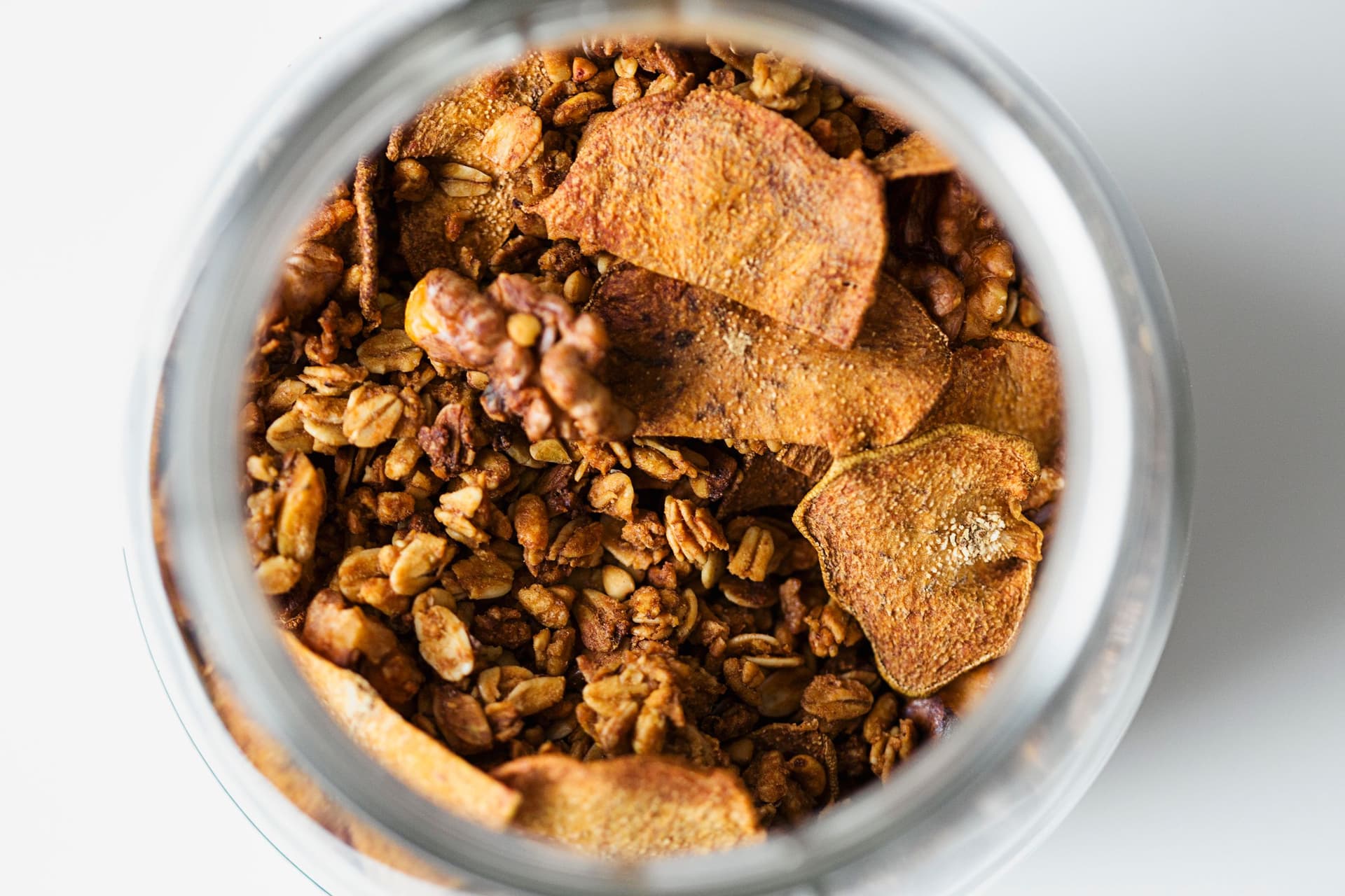 Jar of golden brown granola with dried pear slices viewed from above.