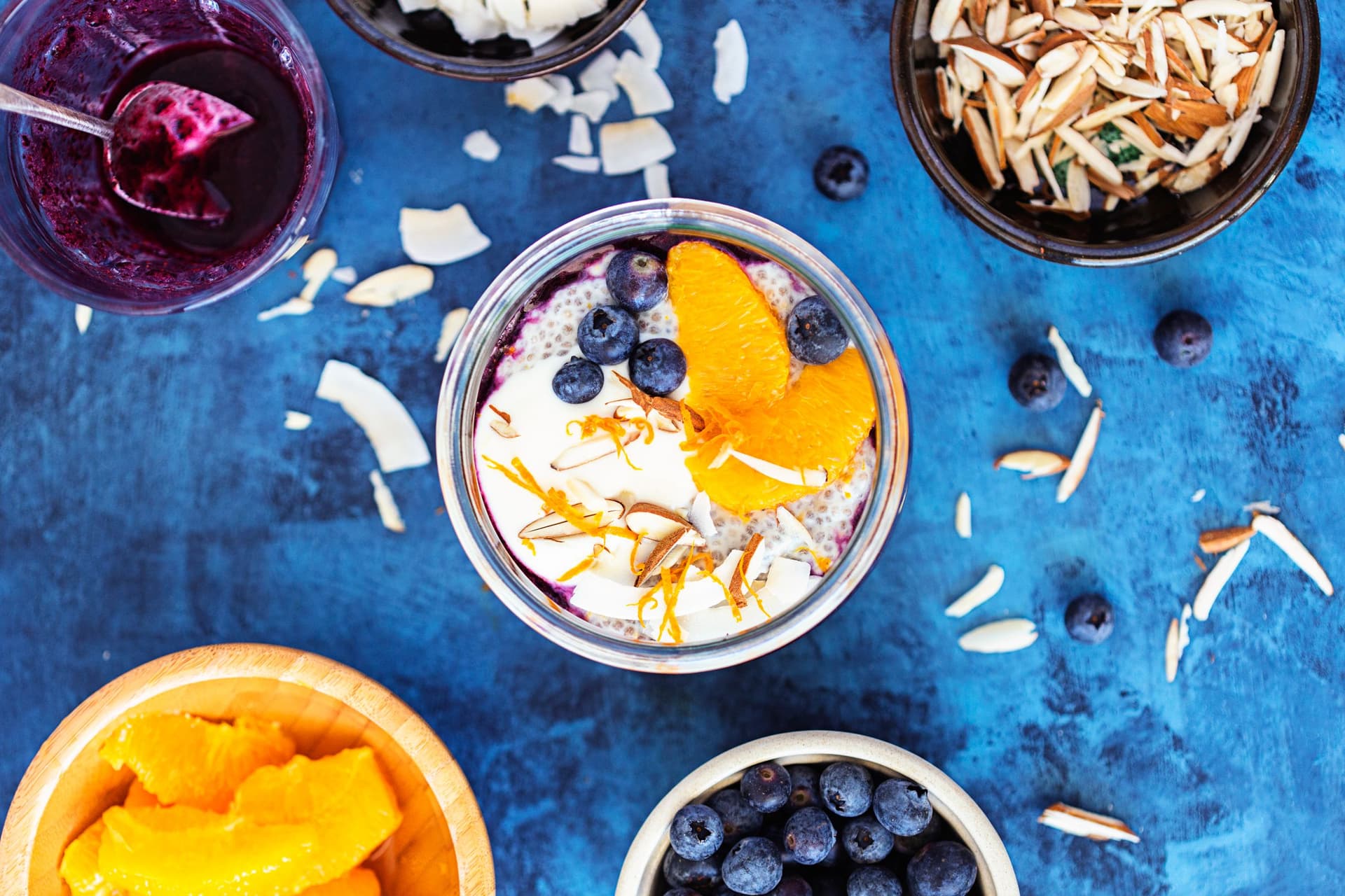 Chia pudding topped with orange slices, blueberries, coconut flakes and almonds, viewed from above.